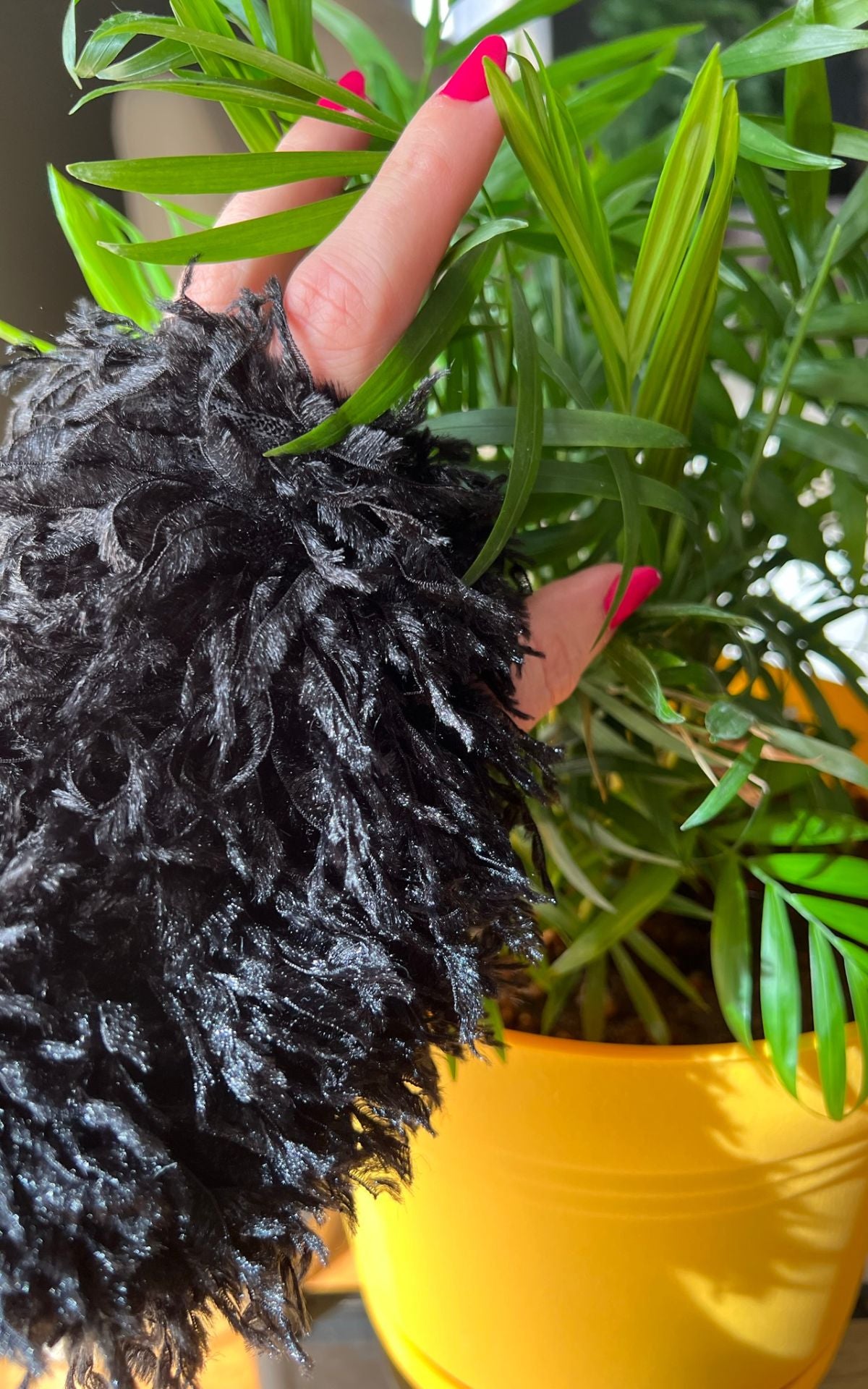 woman&#39;s wearing faux fur fingerless gloves in Black Swan and she is touching a houseplant. Made in Seattle, WA, USA. Pandemonium Seattle.