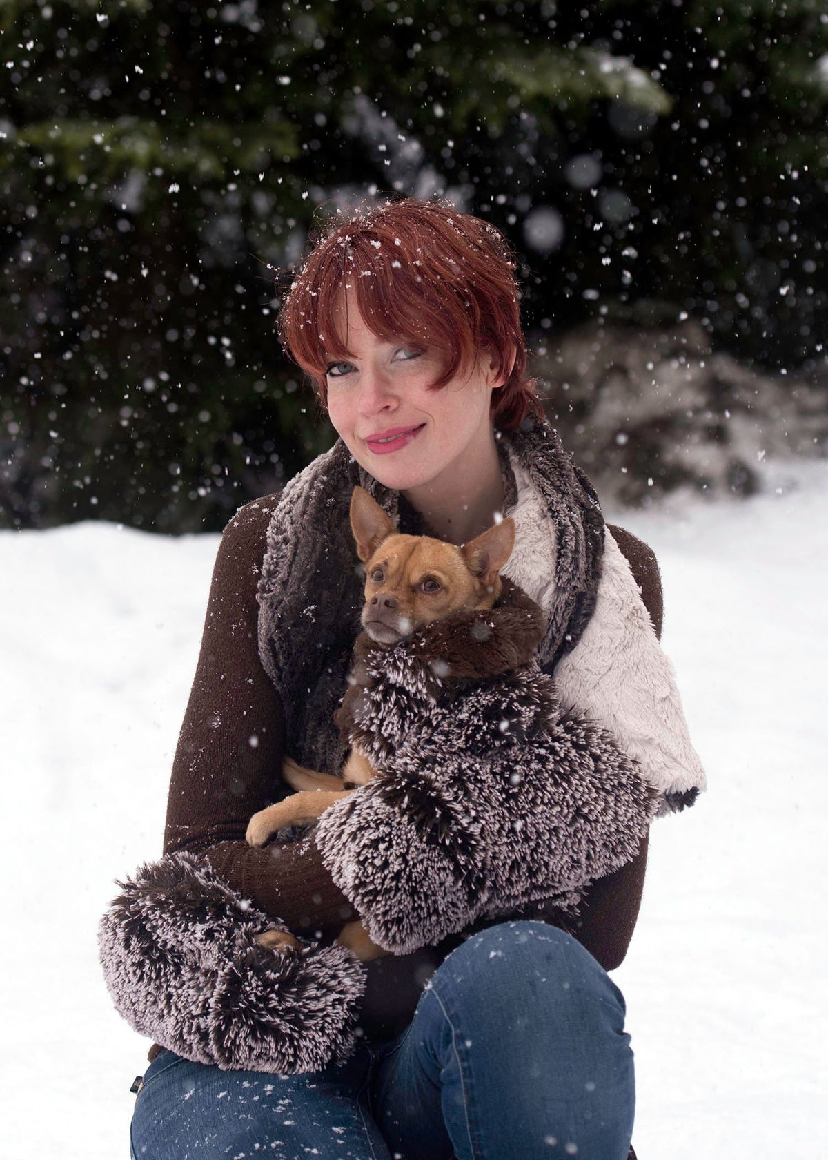 Model in snow holding a Chihuahua wearing Designer Handmade reversible Dog Coat crouching in front of trees| Brown Fox Long hair Luxury Faux Fur | Handmade by Pandemonium Millinery Seattle, WA USA