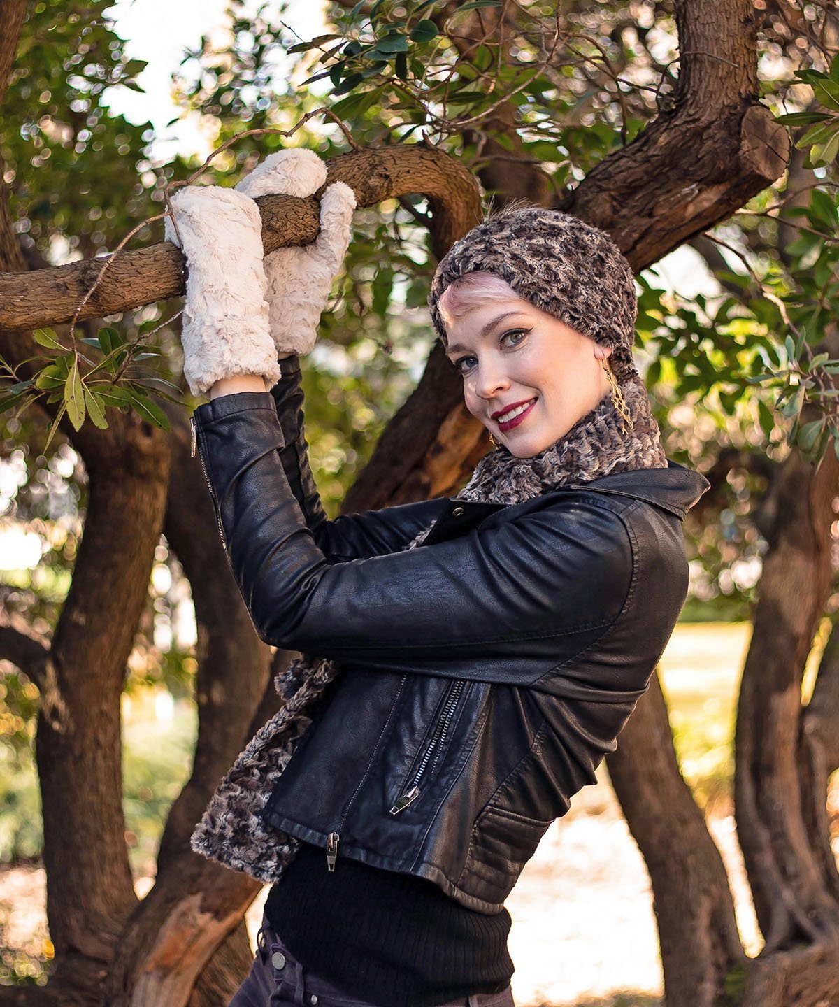model hanging off tree in wearing a black leather jacket and faux fur Headband, scarf and mittens | Calico, brown, chocolate and Ivory Faux Fur | Handmade by Pandemonium Millinery Seattle, WA USA
