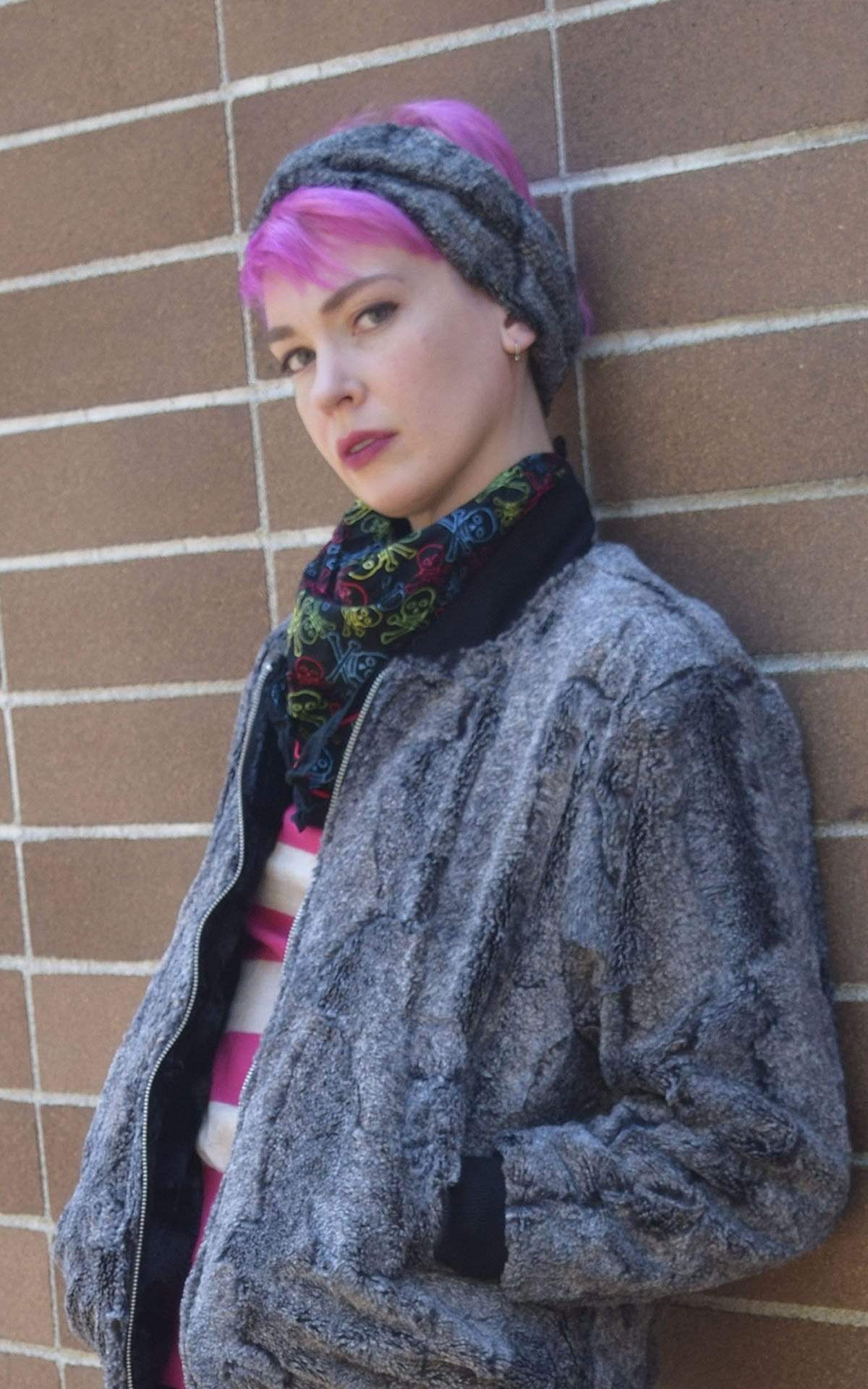 Model wearing of Headband, and matching Bomber Jacket leaning against brick wall | Nimbus, Black and Gray Faux Fur | Handmade by Pandemonium Millinery Seattle, WA USA