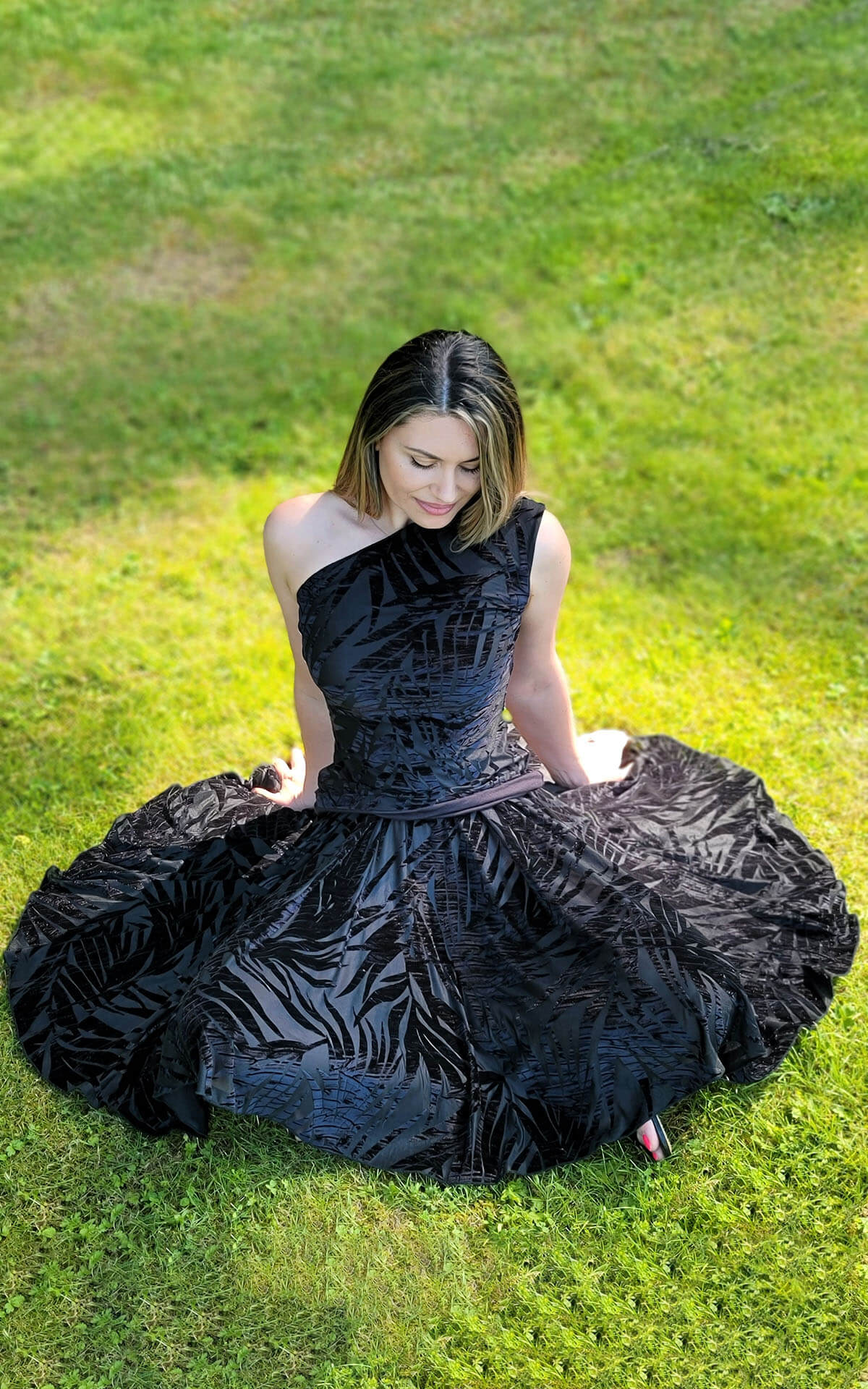 Model sitting in grass wearing a Circle Skirt in Midnight Palm paired with a matching Top