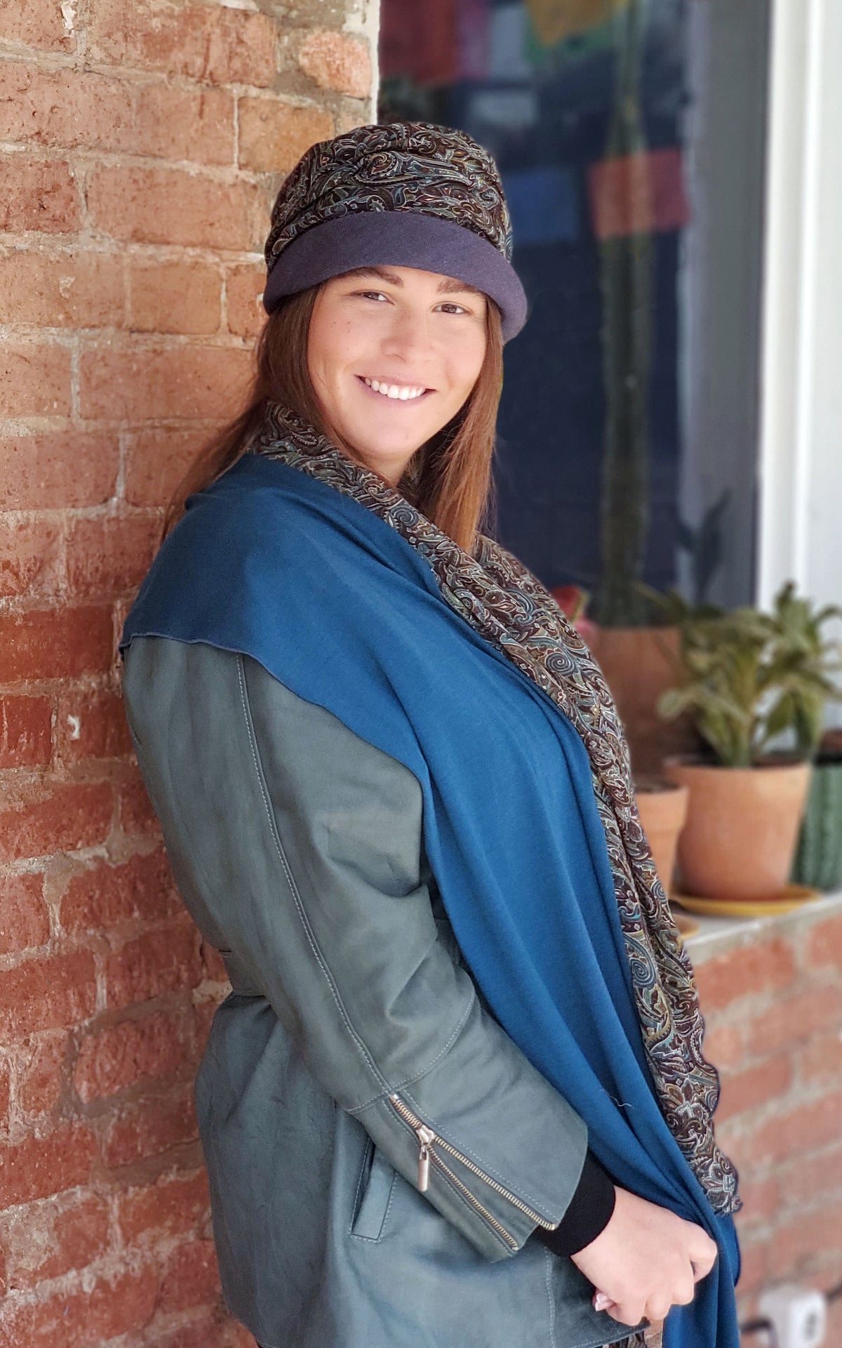 Model against a brick wall wearing Ana 1920’s cloche style hat and matching  Handkerchief Scarf, Wrap | Peacock Paisley Chiffon in blue, greens, and browns | Handmade in Seattle WA | Pandemonium Millinery