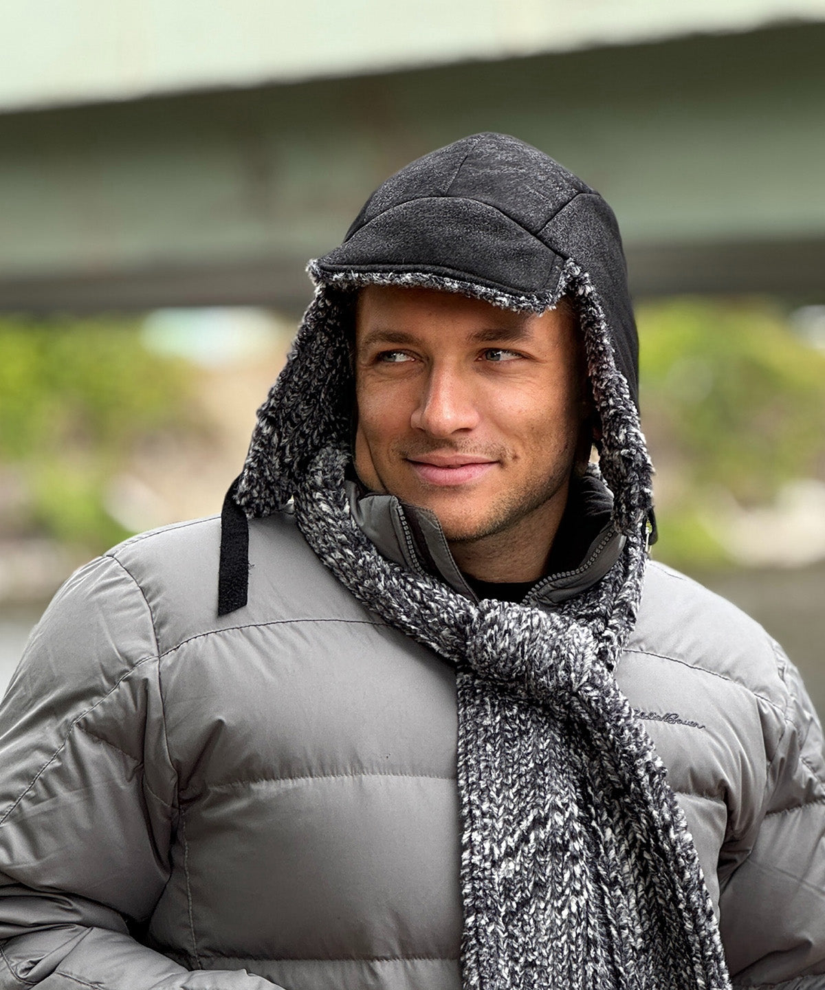 A man wearing an Aviator Hat or Cap in Vegan Leather Rustic Noir with Cozy Cable lining. The ear flaps are down and the strap is not closed. He's wearing a matching Skinny Scarf in Cozy Cable. Made in Seattle, WA, USA by Pandemonium Seattle.