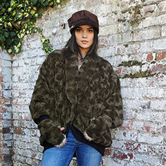 woman standing by brick wall wearing an olive green faux fur oversize coat handmade in USA by Pandemonium Seattle