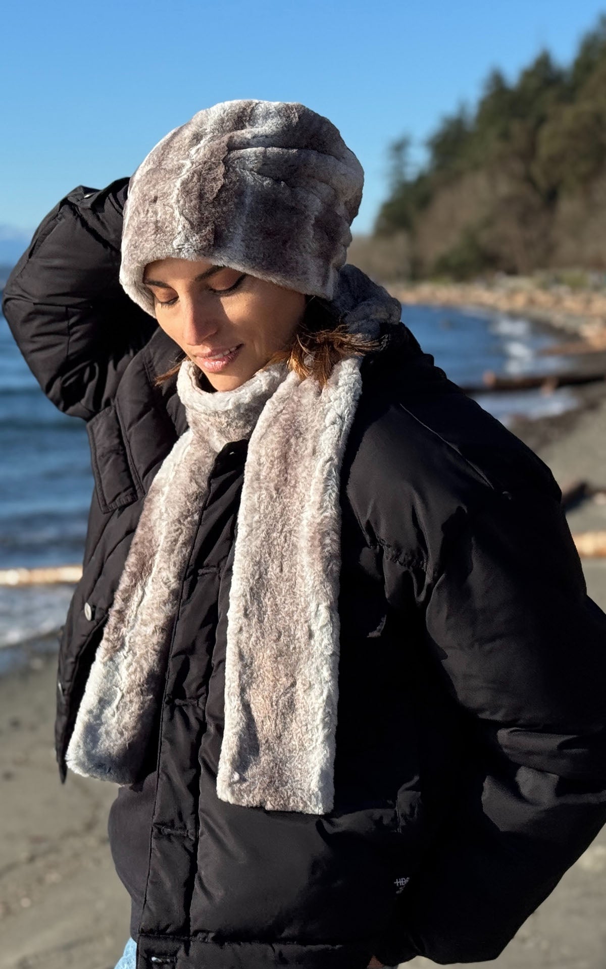 A woman wearing the Cuffed Pillbox and matching Skinny Classic Scarf in Driftwood Faux Fur, as she walks along the beach in Seattle. Made in Seattle, WA, USA by Pandemonium Seattle.