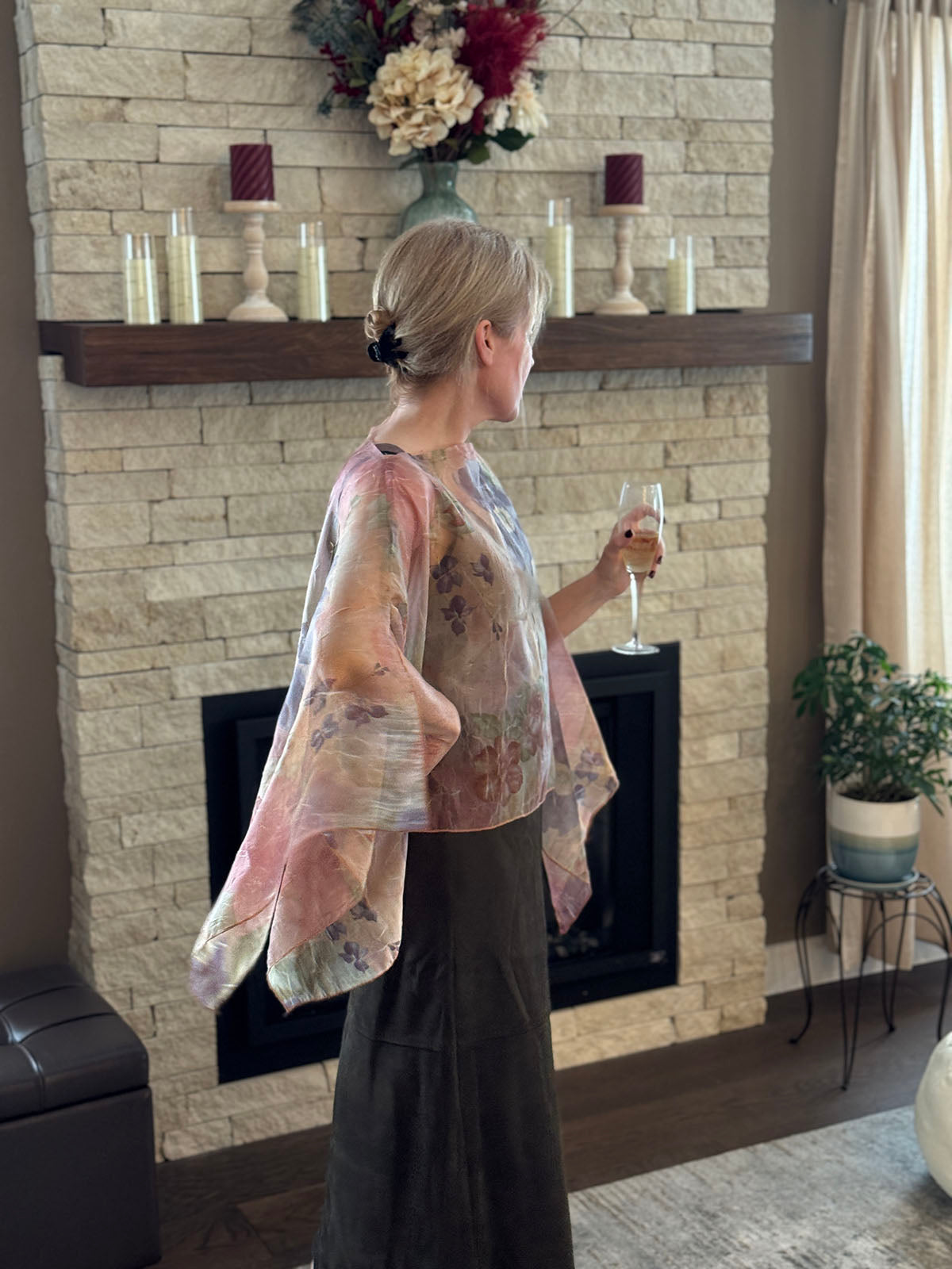 Woman wearing a Coastal Garden Bayberry Poncho by a fireplace. Made in Seattle, WA, USA by Pandemonium Millinery.
