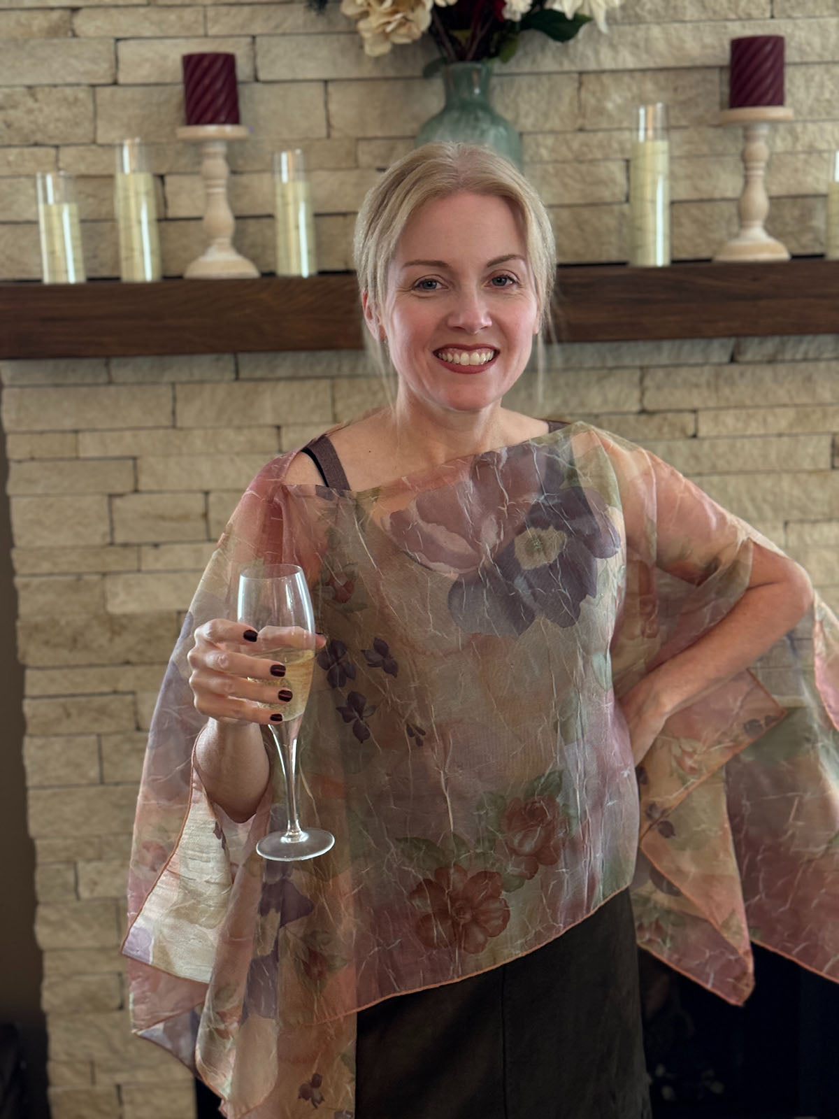 Woman wearing a Coastal Garden Bayberry Poncho by a fireplace. Made in Seattle, WA, USA by Pandemonium Millinery.
