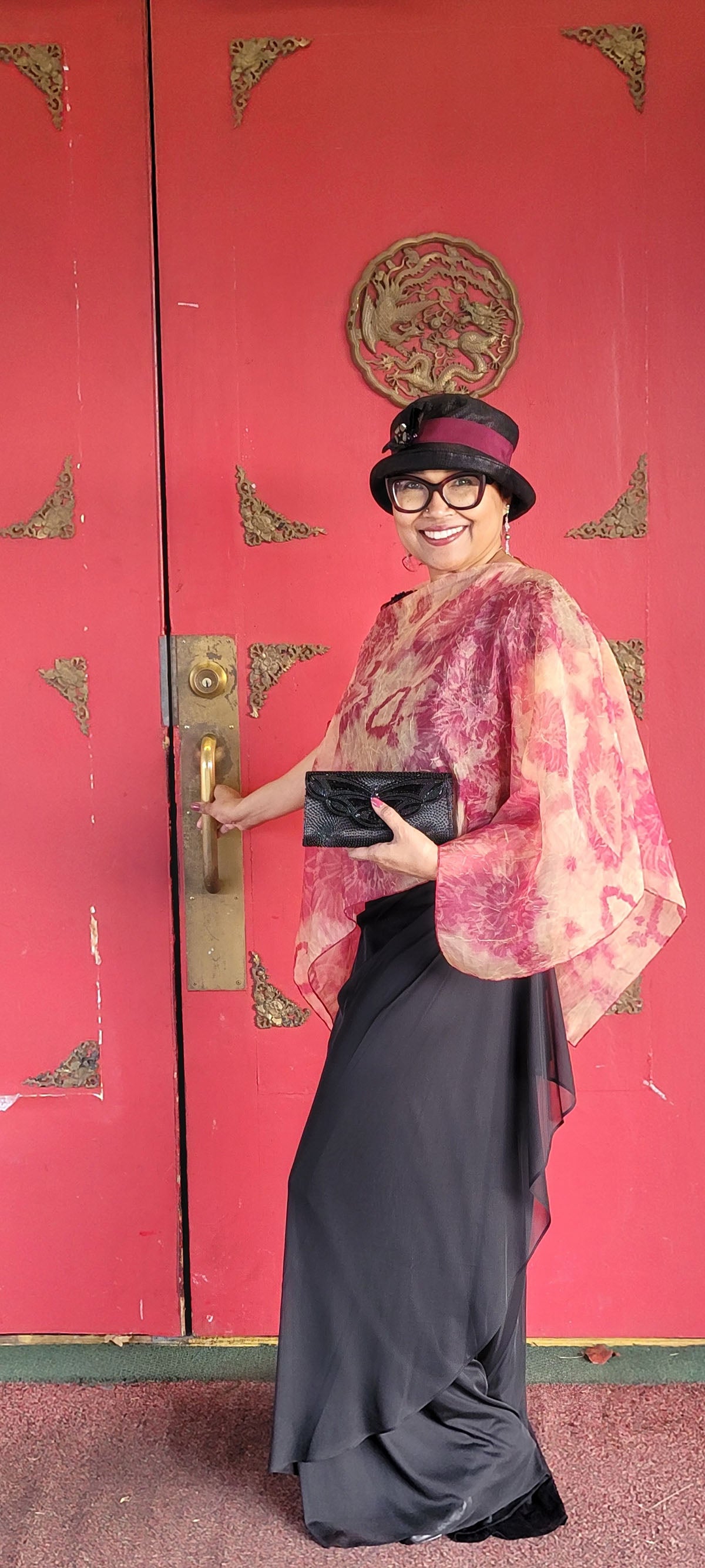 Woman wearing the Coastal Garden Poncho in Coral by a doorway. Made in Seattle, WA, USA by Pandemonium Millinery.