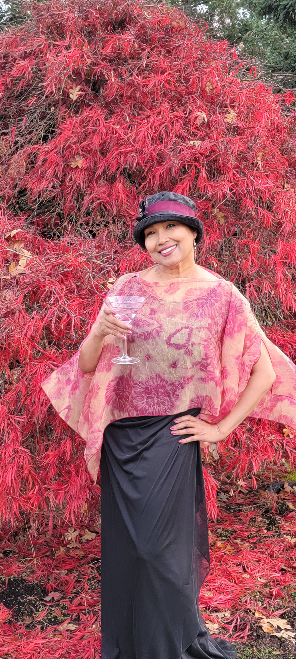 Woman wearing the Coastal Garden Poncho in Coral at a garden party. Made in Seattle, WA, USA by Pandemonium Millinery.
