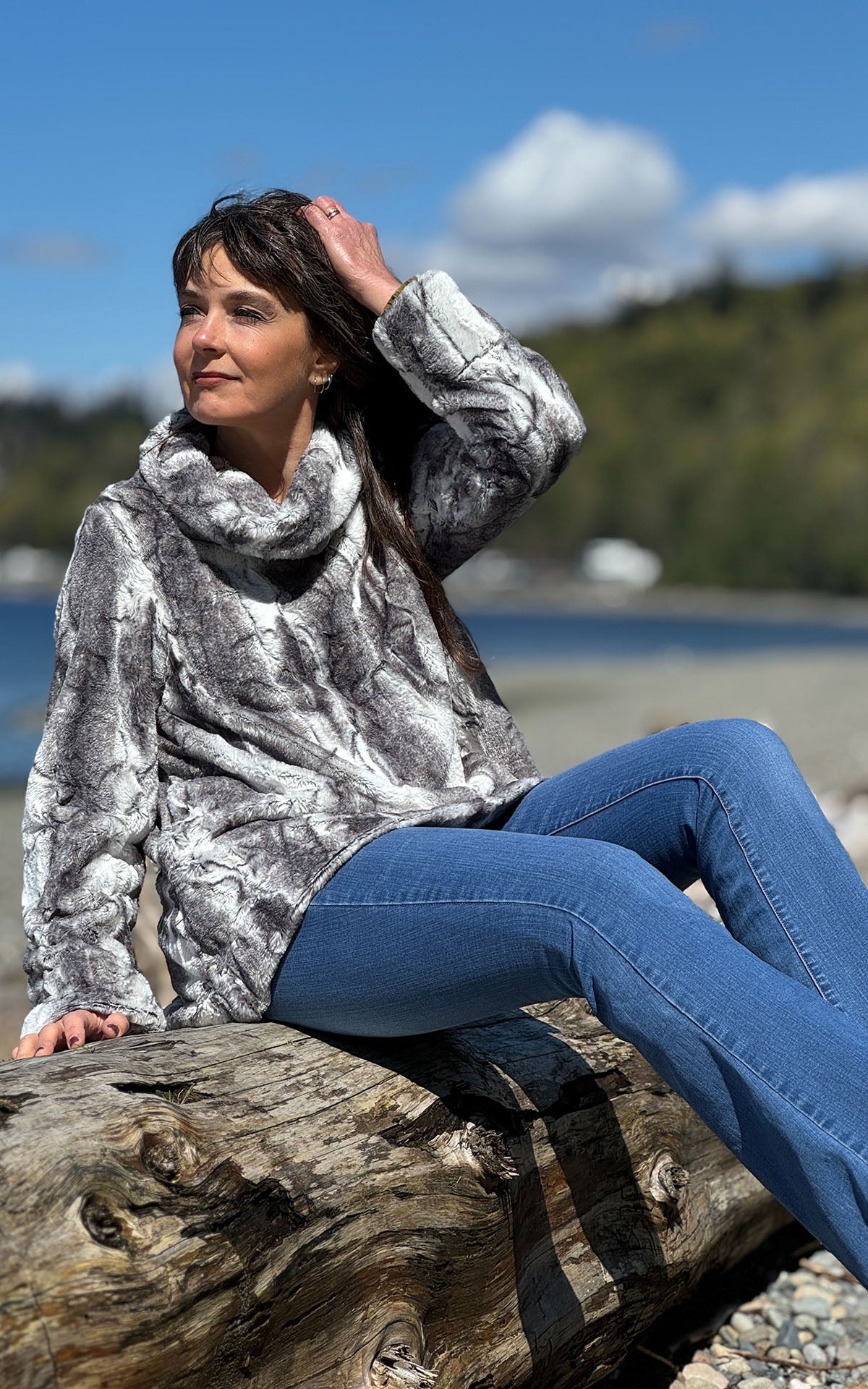 A woman sitting a piece of driftwood featuring a Cowl Top in Smoke Show Faux Fur. Handmade in Seattle, WA , USA by Pandemonium Millinery