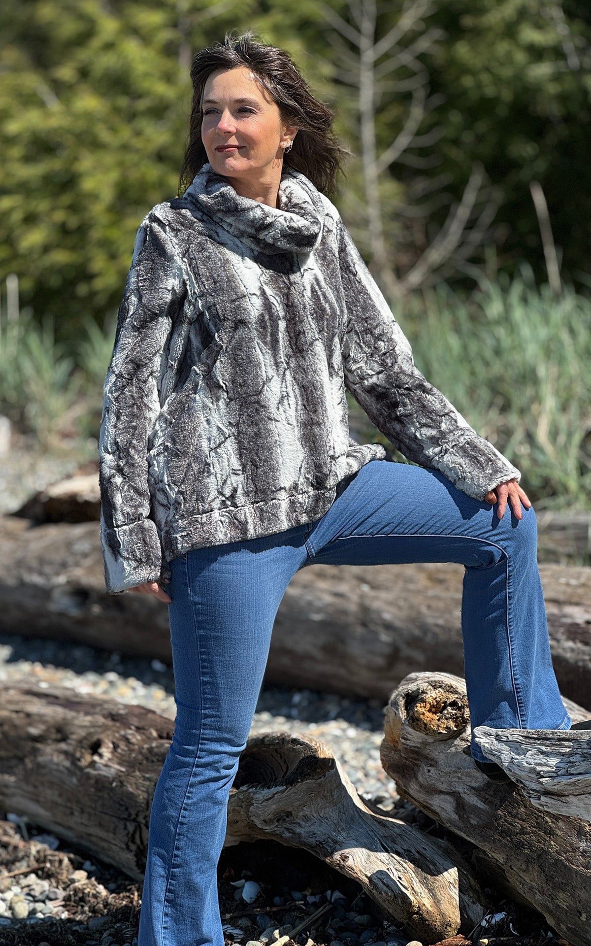 A woman standing with one foot on a piece of driftwood wearing a Cowl Top in Smoke Show Faux Fur. Handmade in Seattle, WA , USA by Pandemonium Millinery