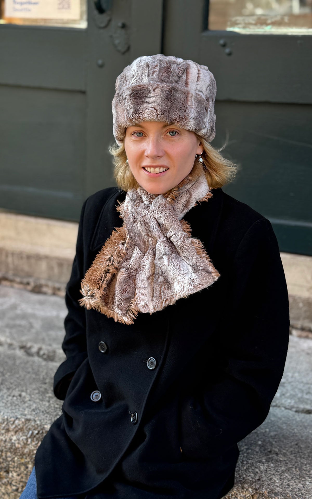 A woman wearing a Cuffed Pillbox Hat in Rusty Rock Faux Fur with a matching Pull-Thru Scarf in Rusty Rock and Red Fox Faux Fur, over a black peacoat. Made in Seattle, WA, USA by Pandemonium Seattle.