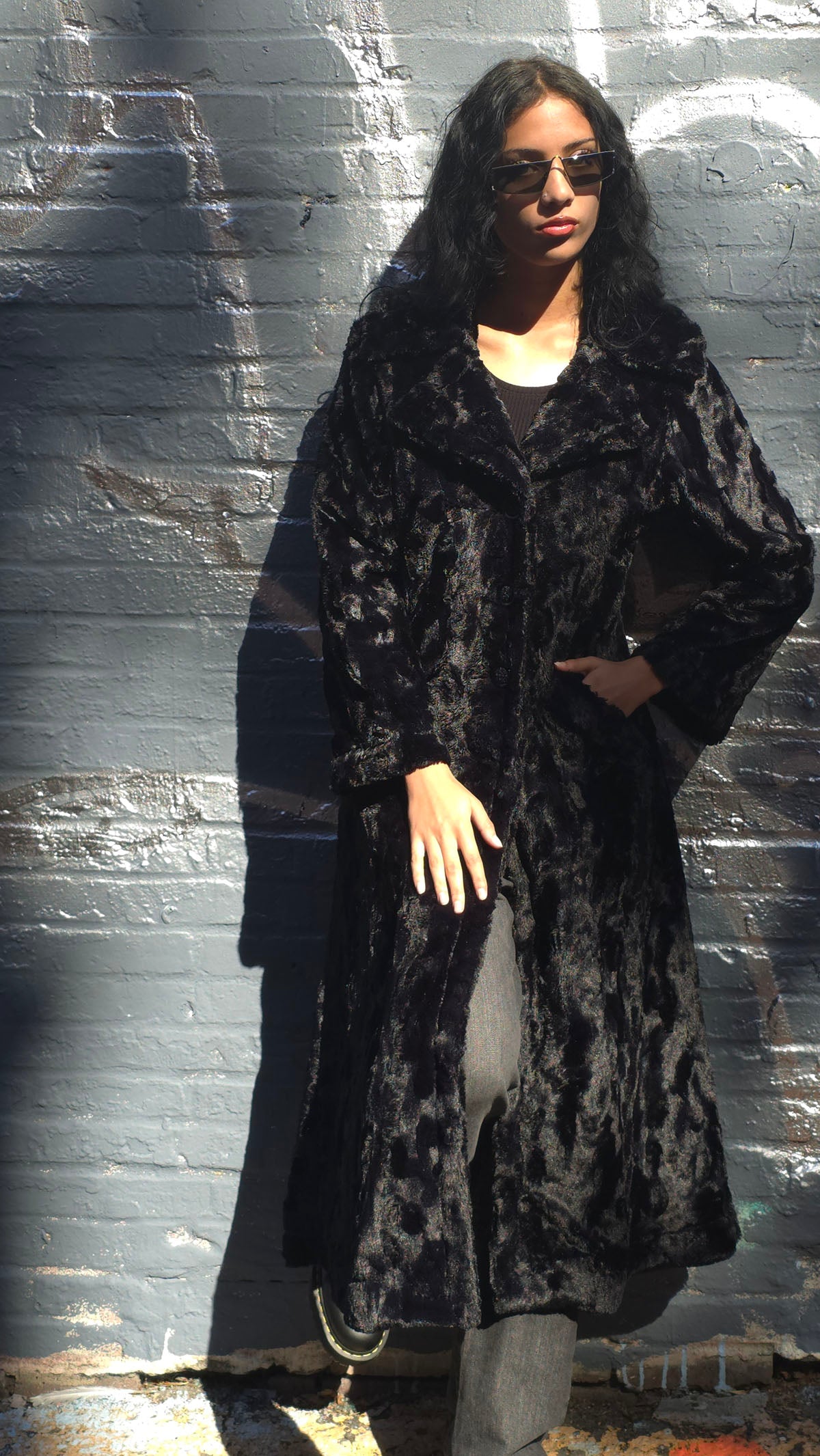 Woman wearing the Hayworth Coat in Cuddly Black standing against a brick wall. Made in Seattle, WA, USA by Pandemonium Seattle.