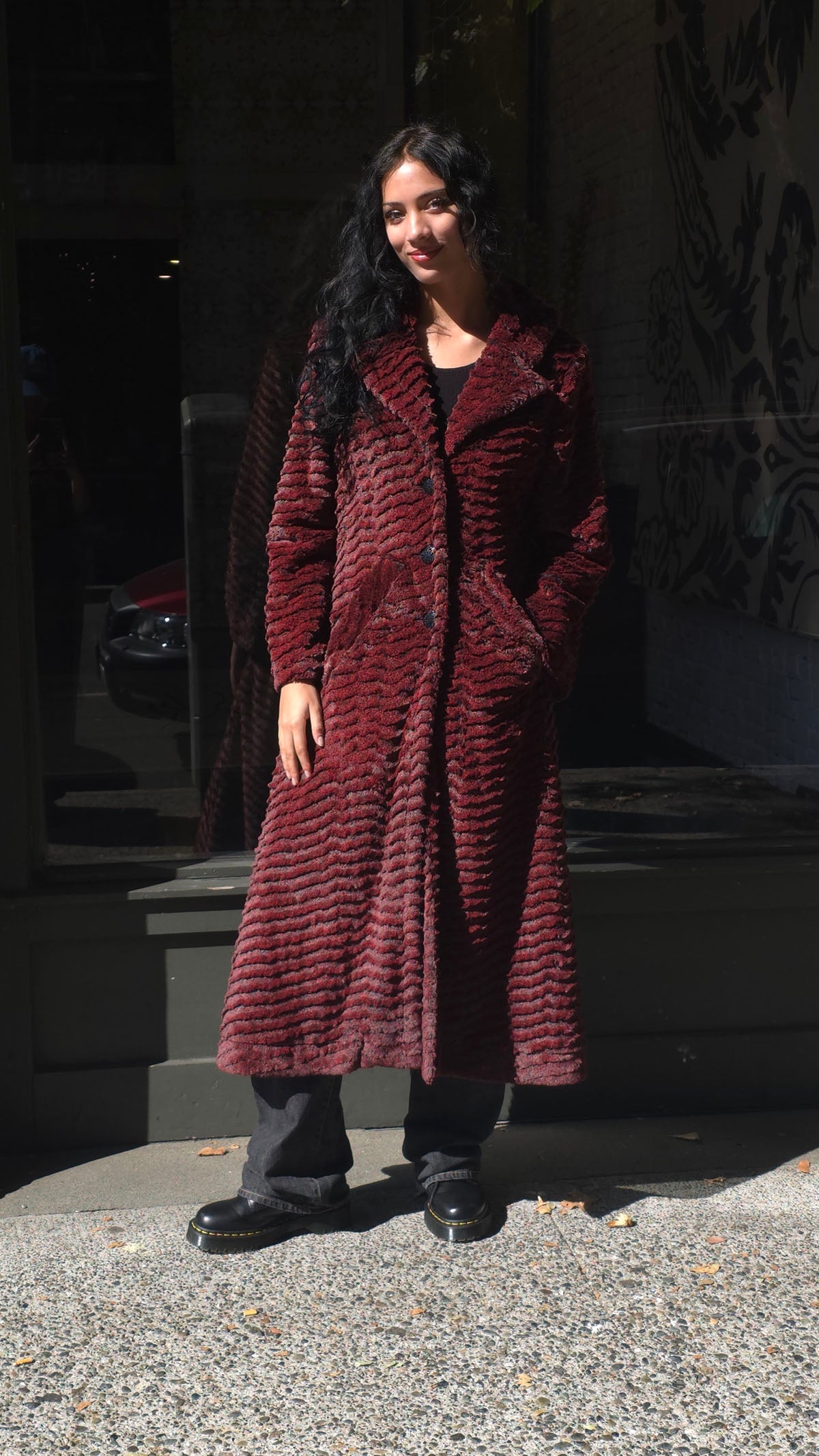 Woman wearing the Hayworth Coat in Desert Sand Crimson, with one hand in pocket. Made in Seattle, WA, USA by Pandemonium Seattle.