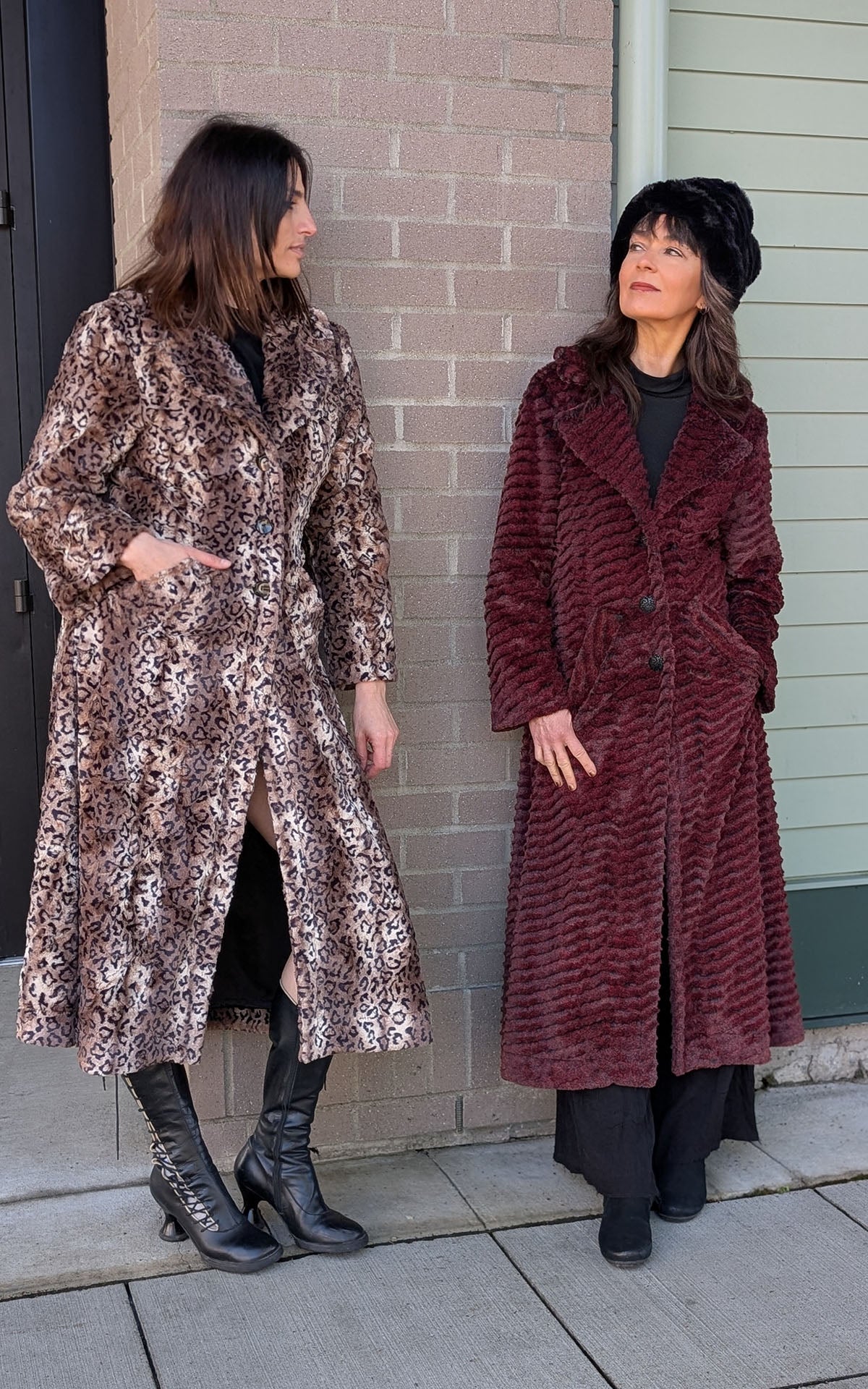 Two women leaning against a building wearing the Hayworth coats, one in Carpathian Lynx (Left) and the other in Deseret Sand in Crimson Faux Fur (Right). Handsewn in Seattle WA, USA by Pandemonium Seattle