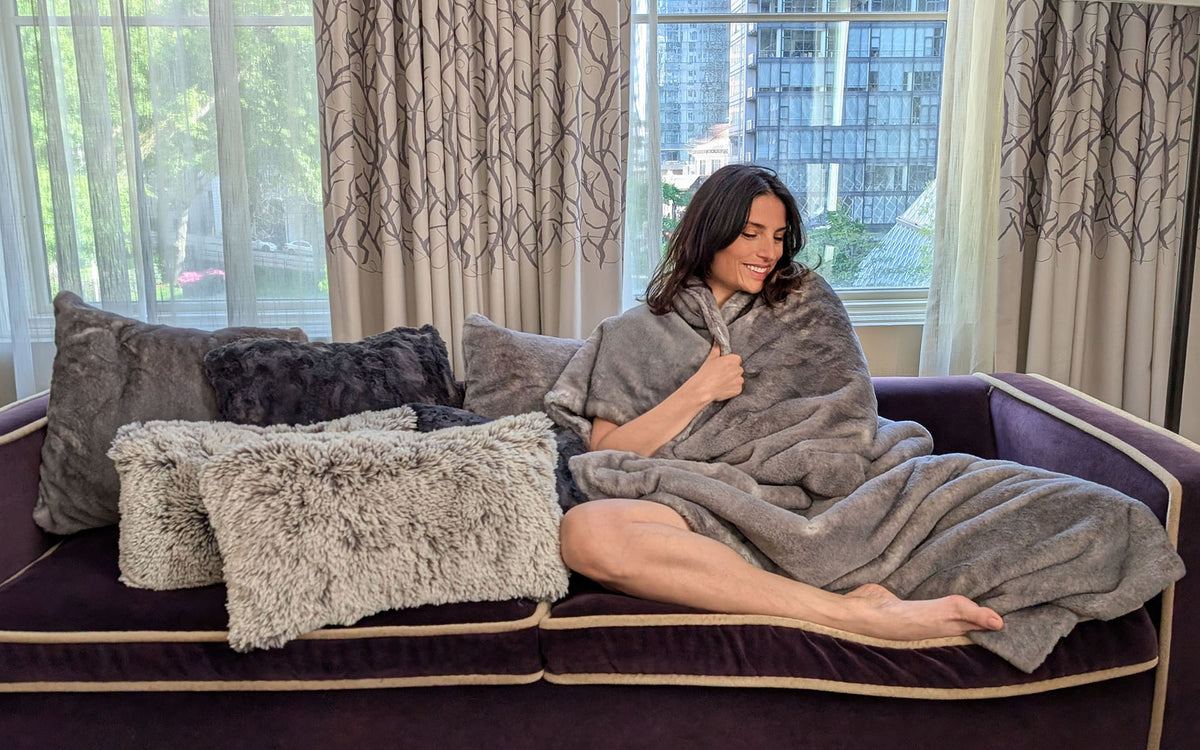 Woman wrapping herself in the Coastal Plush Olympic Fog Throw Blanket, with matching throw pillows. Made in Seattle, WA, USA by Pandemonium Seattle.