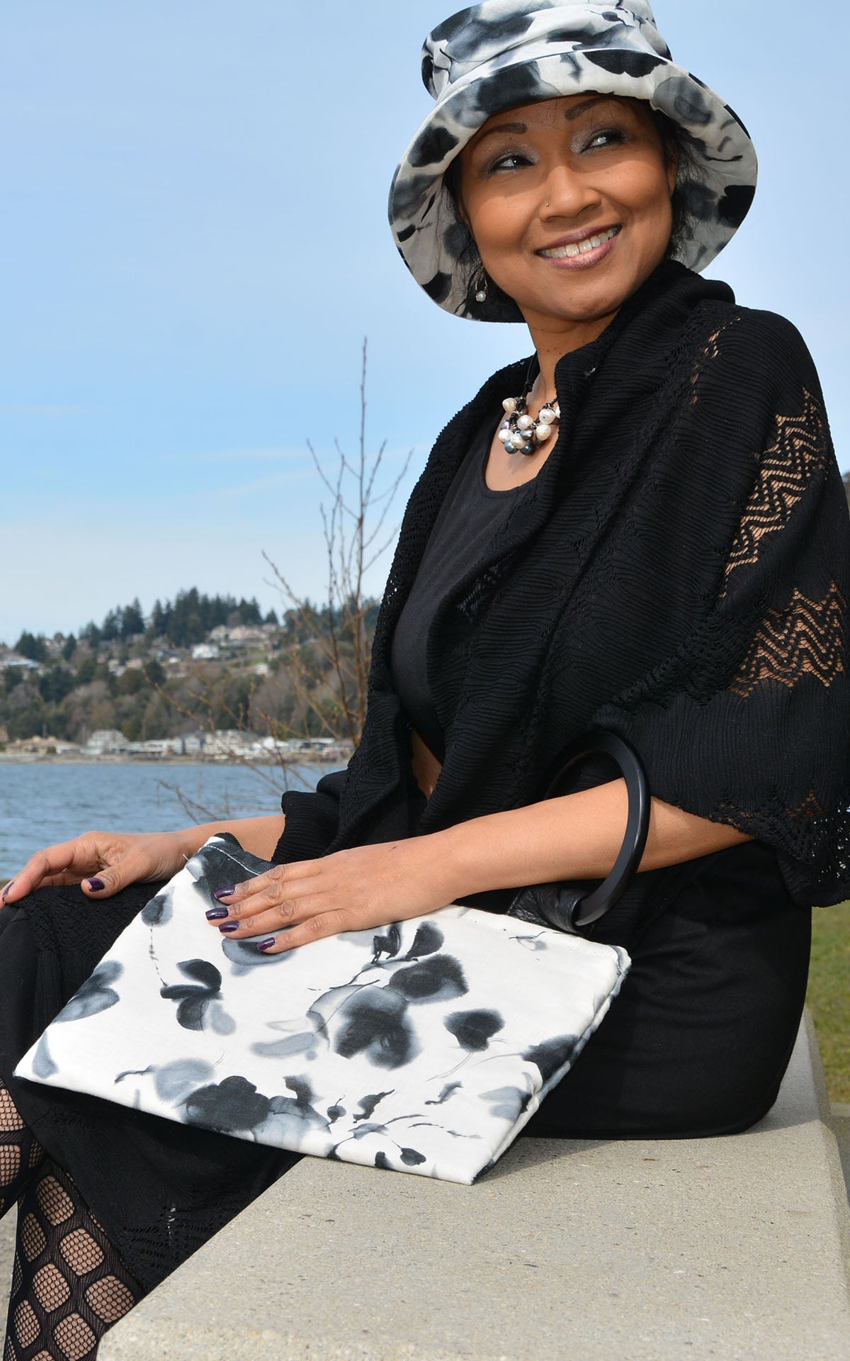 Woman sitting by a lake holding a black and white patterned clutch
