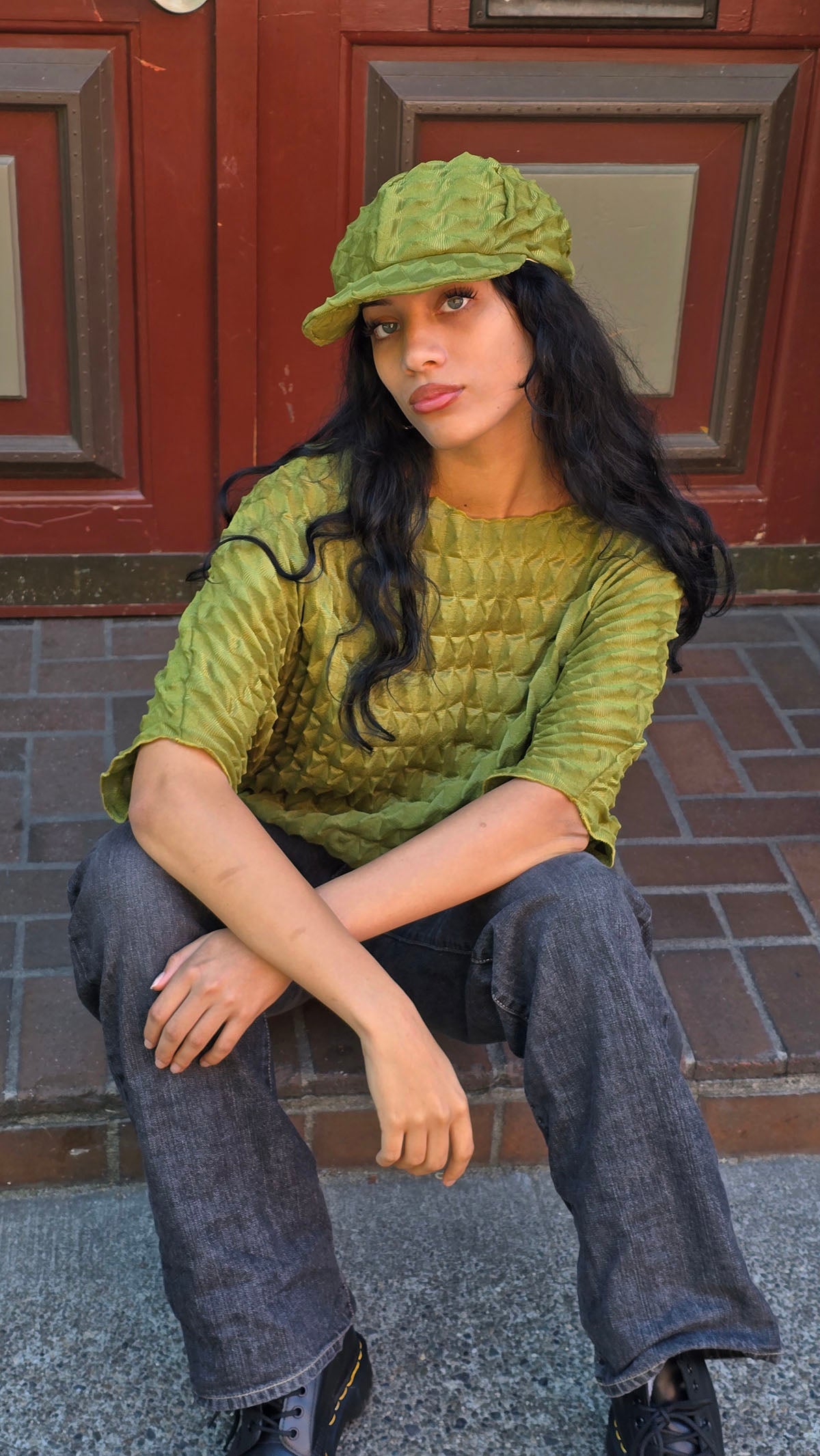 LYC Fractal Dianne Cap in Avocado worn by a woman sitting on a stoop. Made in Seattle, WA, USA by Pandemonium Seattle.