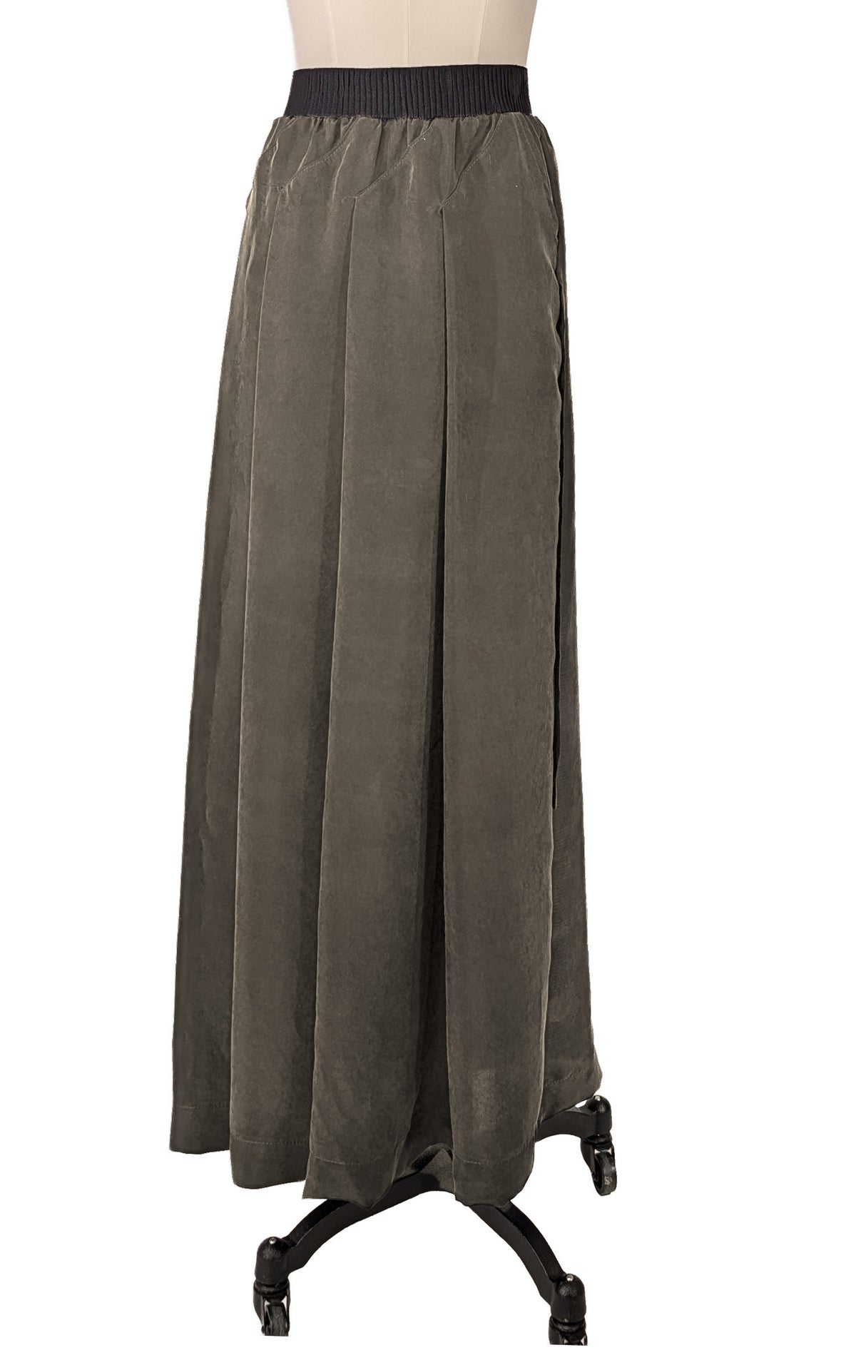 A dark olive green pleated maxi skirt with a black ribbed waistband, displayed on a dress form stand against a white background. Made in Seattle, WA, USA by Pandemonium Seattle.