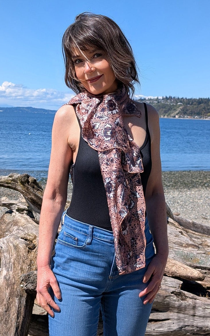 Woman standing on a beach wearing the Lumina Poncho in Hippy Chick, styled in front like a scarf. Made in Seattle, WA, USA by Pandemonium Seattle.