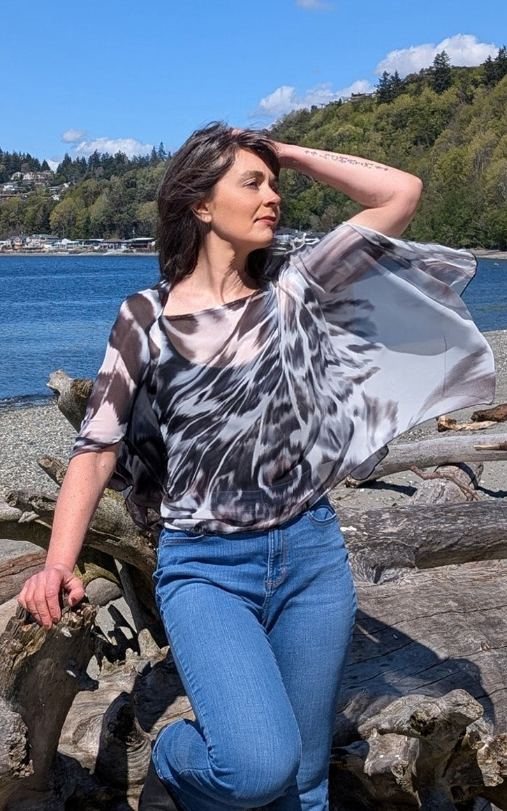 Woman at the beach wearing the Lumina Poncho in Social Butterfly. Made in Seattle, WA, USA by Pandemonium Seattle.