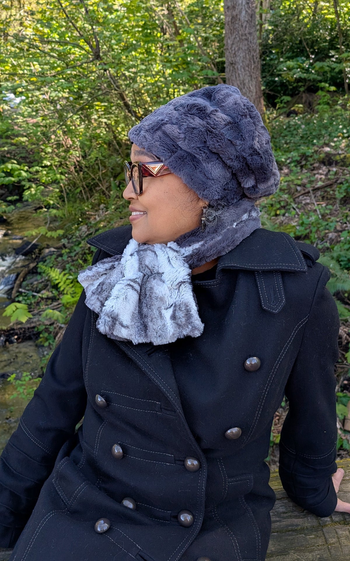 Woman in the forest is wearing a Cuffed Pillbox in Smoky with a Pull- Thru Scarf in Smoke Show Faux Fur. Handmade in Seattle, WA, USA. By Pandemonium Seattle.    