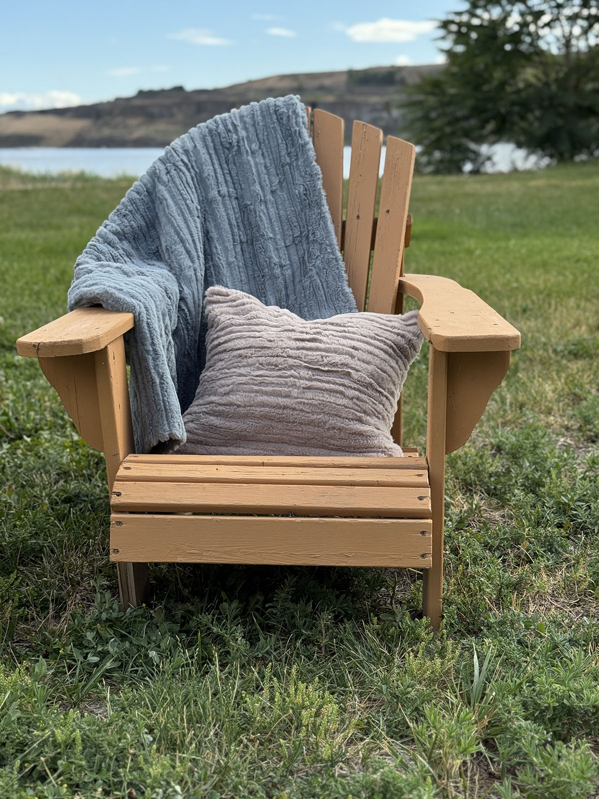 Cirrus in Blue Mist Standard Throw and our Pillow Sham in Cirrus in Honey, over a chair by a lake. Hand sewn in Seattle, Washington by Pandemonium Seattle.