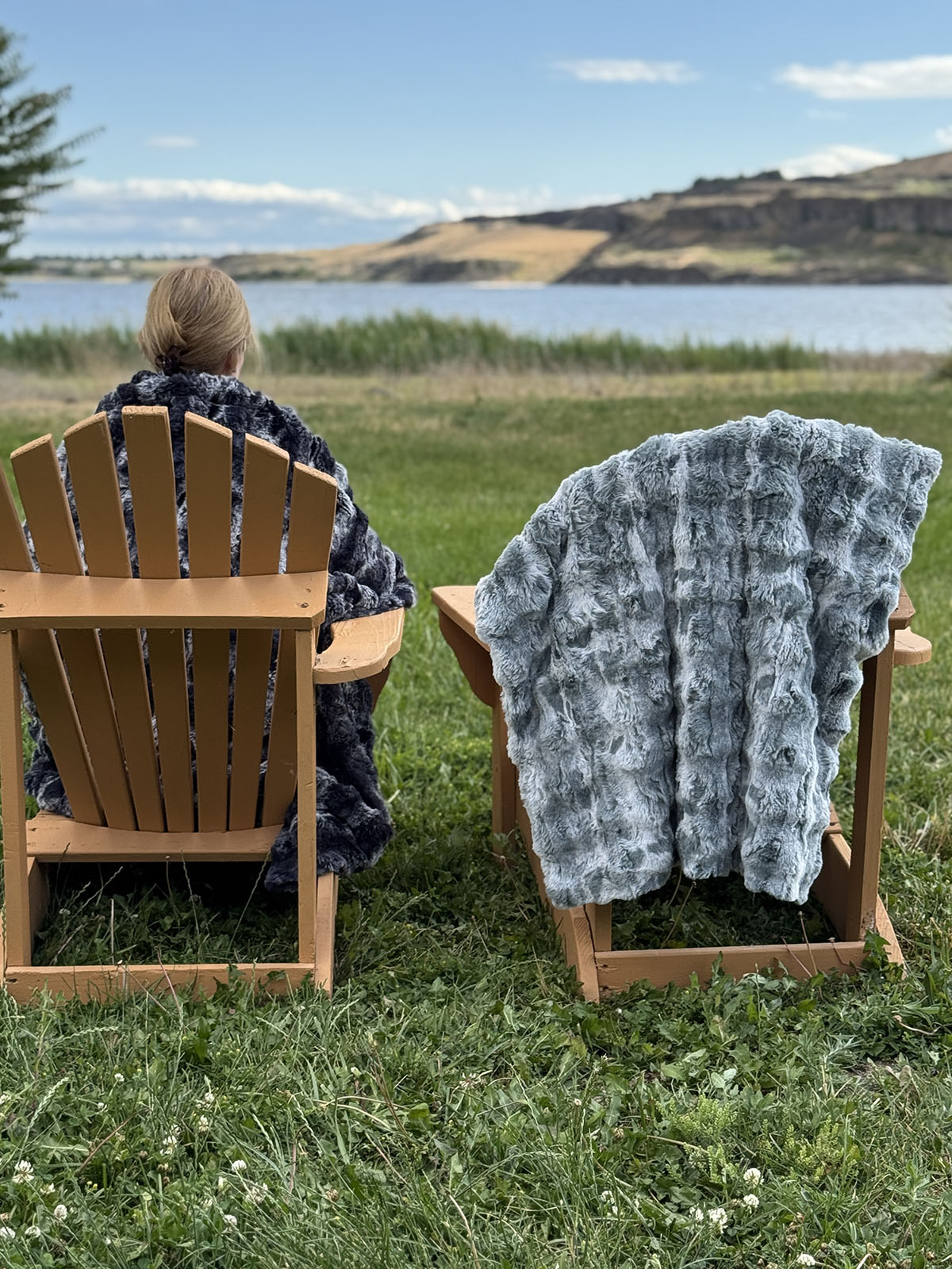 Woman with the Cloudwalk Shadow Throw blanket wrapped around her. The Cloudwalk Blue Mist Throw blanket is draped over the chair beside her. Made in Seattle, WA, USA by Pandemonium Seattle.