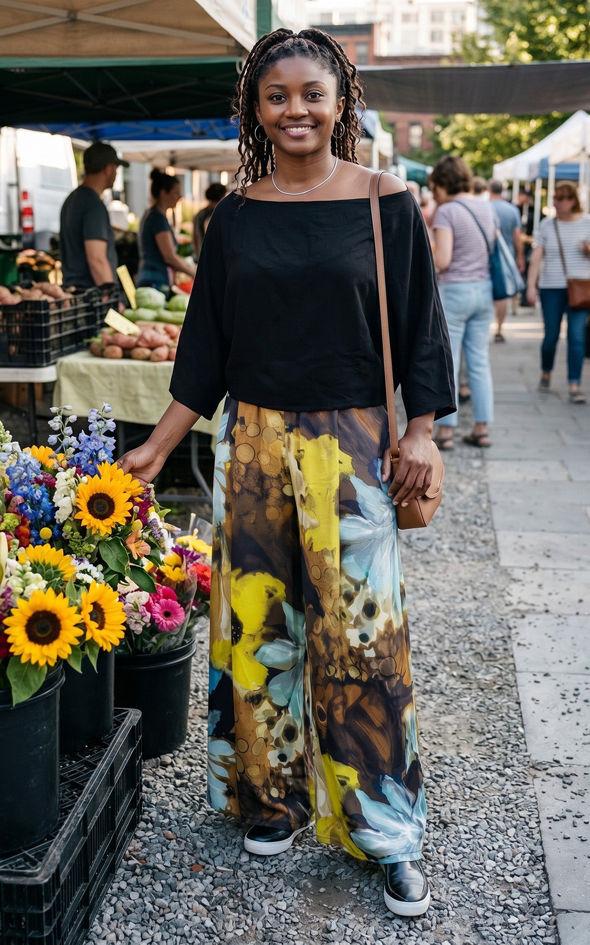 A woman standing by a flower market stand while wearing an Off-the-Shoulder Top in Obisidian with Wide Leg Pants in Fiesta Silk Masquerade for a fun contrast. Made in Seattle, WA, USA by Pandemonium Seattle.