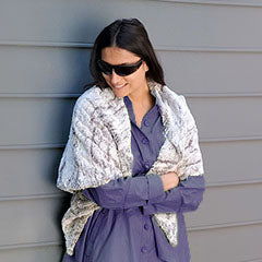 woman in sunglasses standing against gray wall wearing a shawl in ivory and gray green faux fur handmade in USA by Pandemonium Seattle