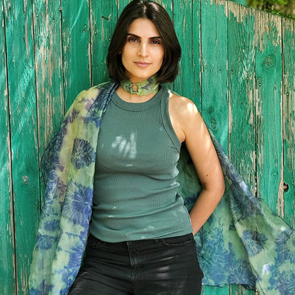 A model wearing a lightweight 'Agave' handkerchief scarf from the Coastal Garden collection, styled as a breezy, breathable accessory for warm weather. standing against a green wall