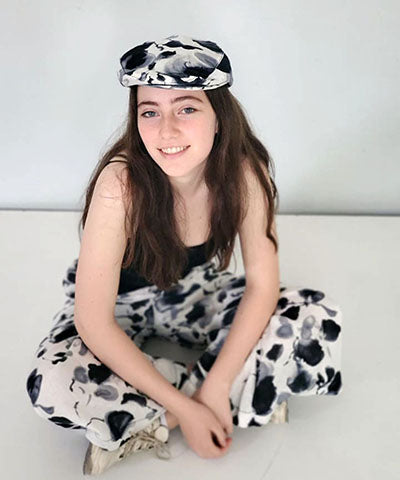 Model sitting on Floor wearing Pandemonium Millinery Charlie Driving Cap and matching Pants | Linen in Black and White Floral | Handmade in Seattle WA
