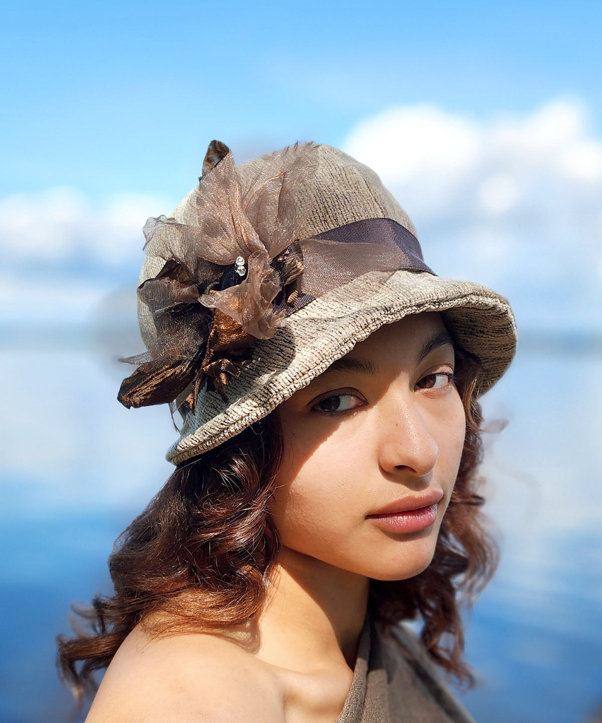 Woman wearing the Grace Cloche Hat in Bongo Beige upholstery fabric. The Grace Cloche Hat in Bongo, is additionally decorated with a fabric flower brooch. Handmade in Seattle, WA, USA by Pandemonium Seattle.