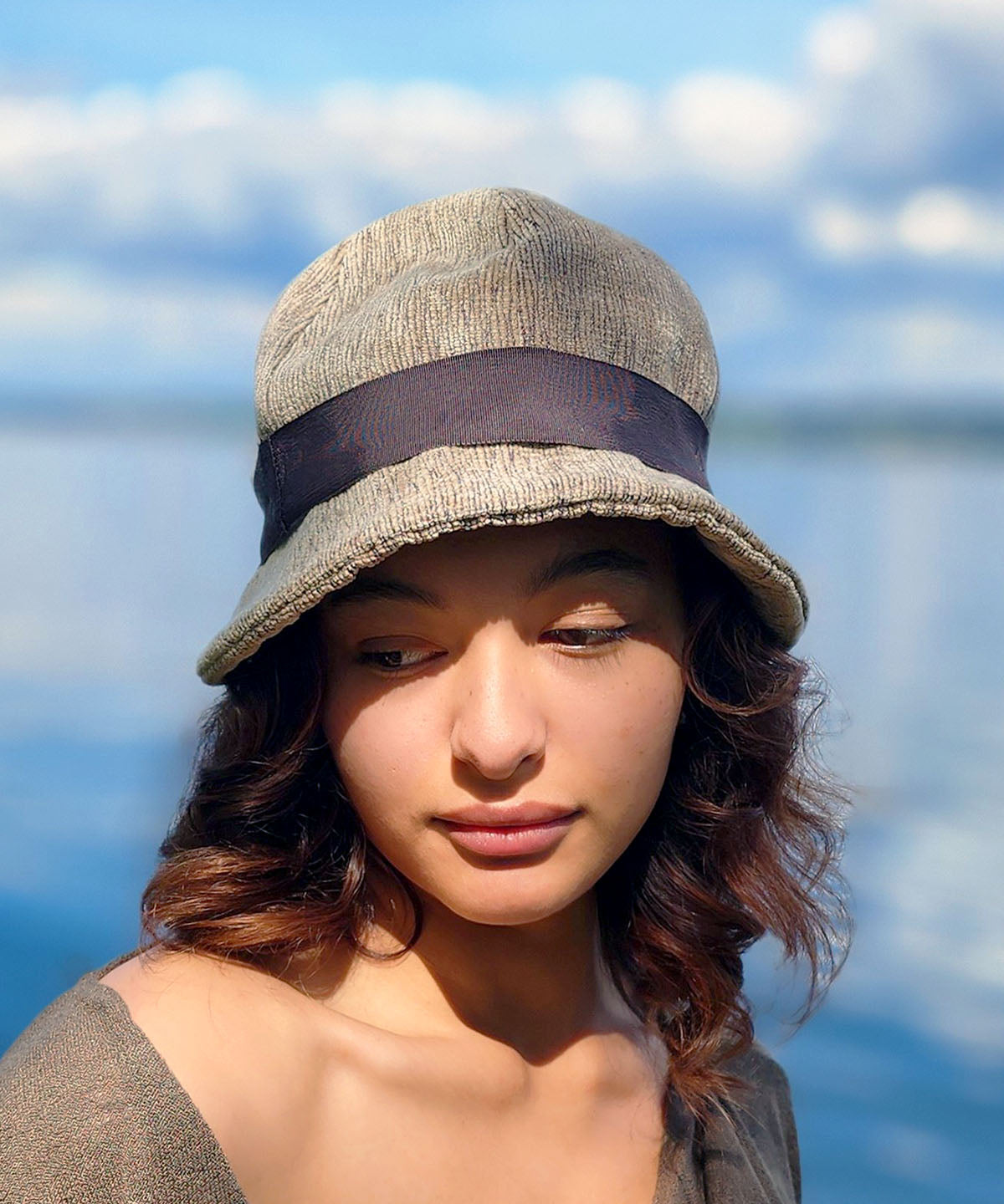 Woman wearing the Grace Cloche Hat in Bongo Beige upholstery fabric. The Grace Cloche Hat in Bongo, is additionally decorated with a fabric flower brooch. Handmade in Seattle, WA, USA by Pandemonium Seattle.