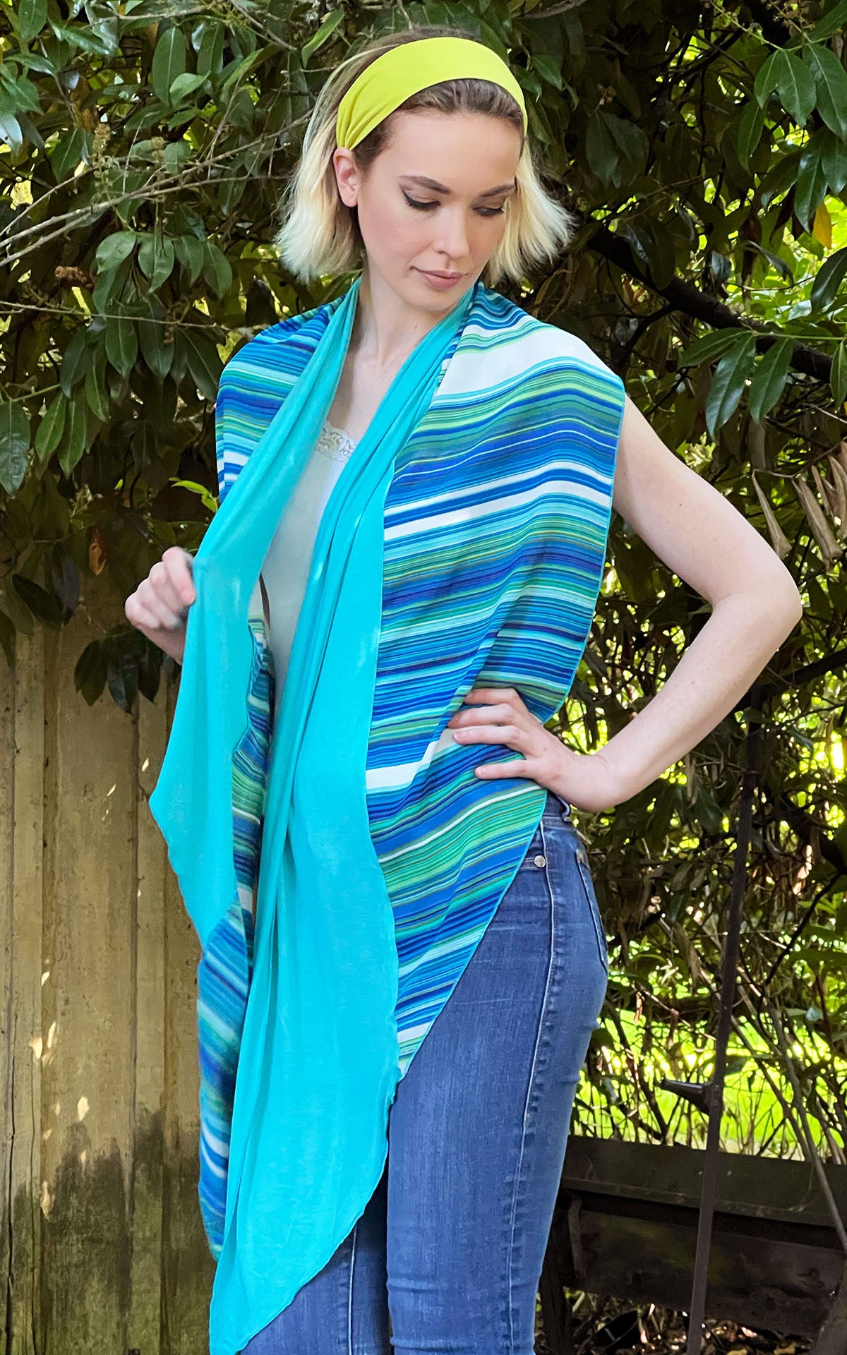 Women standing in front of fence and laurels wearing Handkerchief Scarf, Wrap | Shown in Oceans of Emptiness Jersy knit with Sea Breeze rayon a striped pattern on blues, turquoise, greens, and ivory| Handmade in Seattle WA | Pandemonium Millinery