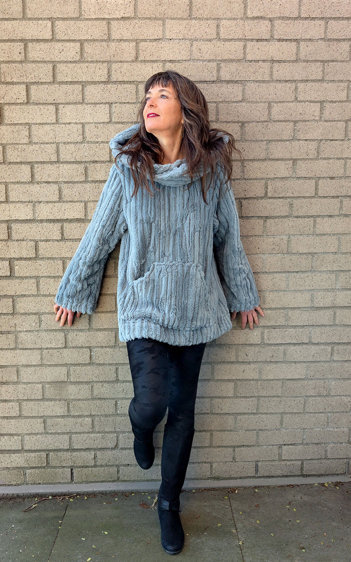 Model leaning on a brick wall wearing Hooded Lounger | Cirrus Faux Fur in Blue Mist | Hood Down View | Handmade in Seattle WA USA | By Pandemonium Seattle