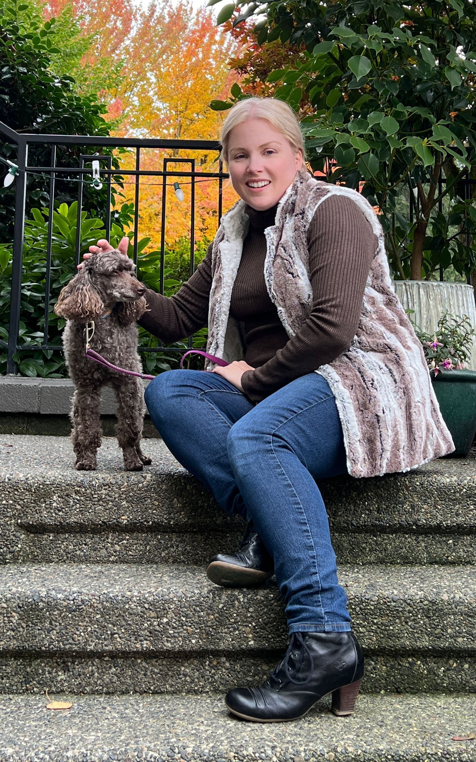 Woman sitting on steps with dog wearing the Short Mandarin Vest in Birch Faux Fur with reversible Cuddly Ivory Faux Fur. Custom made by Pandemonium Seattle.