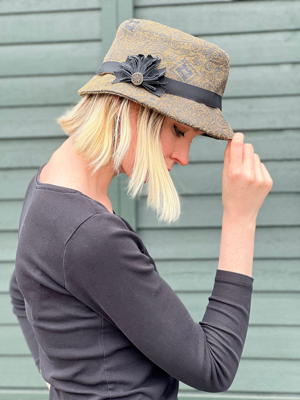 Woman tipping brim of Olivia Fedora Hat in Rubino Upholstery with Custom Grosgrain Brooch | Handmade in Seattle WA | Pandemonium Millinery