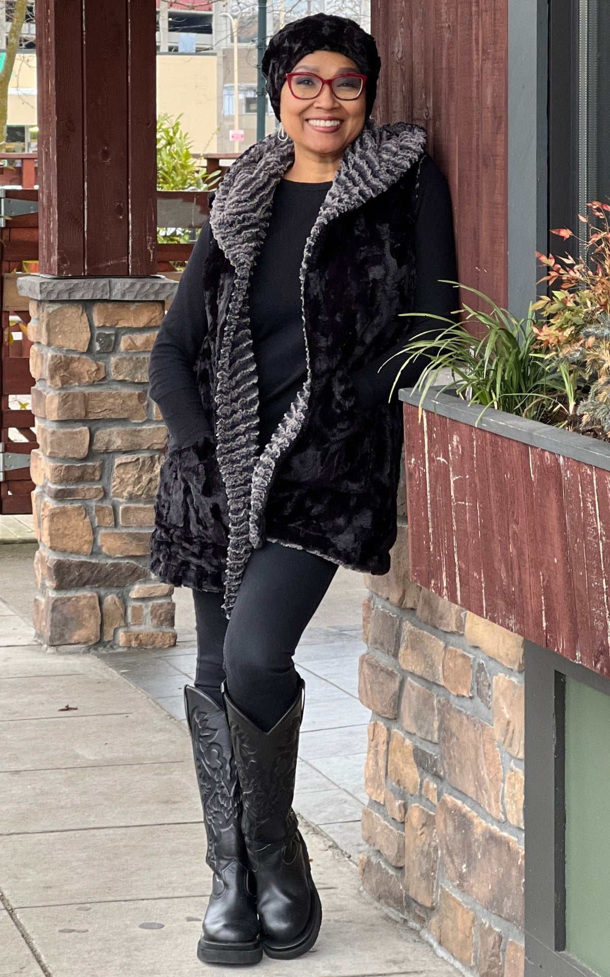 Woman modeling the Oversized Hooded Vest in Cuddly Black faux fur with the reverse color Desert Sand Charcoal. Handmade by Pandemonium Seattle.