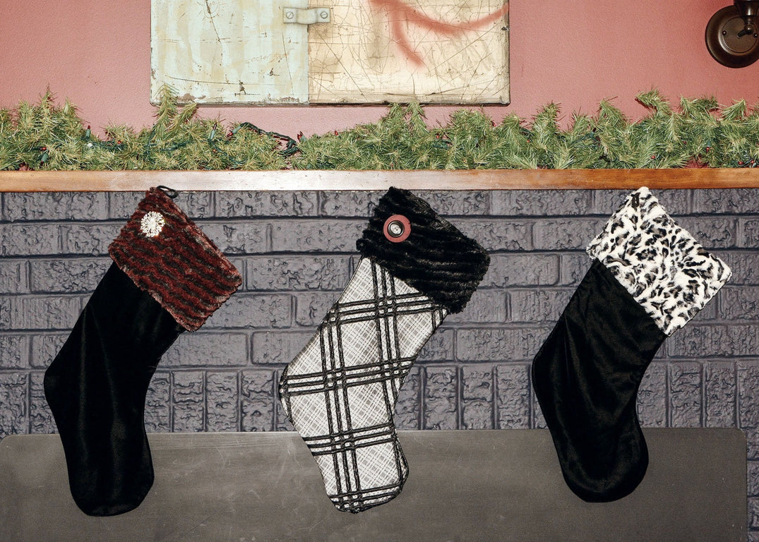 Three Christmas Stockings hanging on Fireplace Mantle | Stocking in Velvet in Black with Desert Sand in Crimson Cuff featuring a Rhinestone Brooch | Stocking in Silver Plaid with Cuddly Black Faux Fur Cuff with a Button Accent | Stocking in Velvet in Back with White Jaguar Faux Fur Cuff | By Pandemonium Seattle | Handmade in Seattle WA US