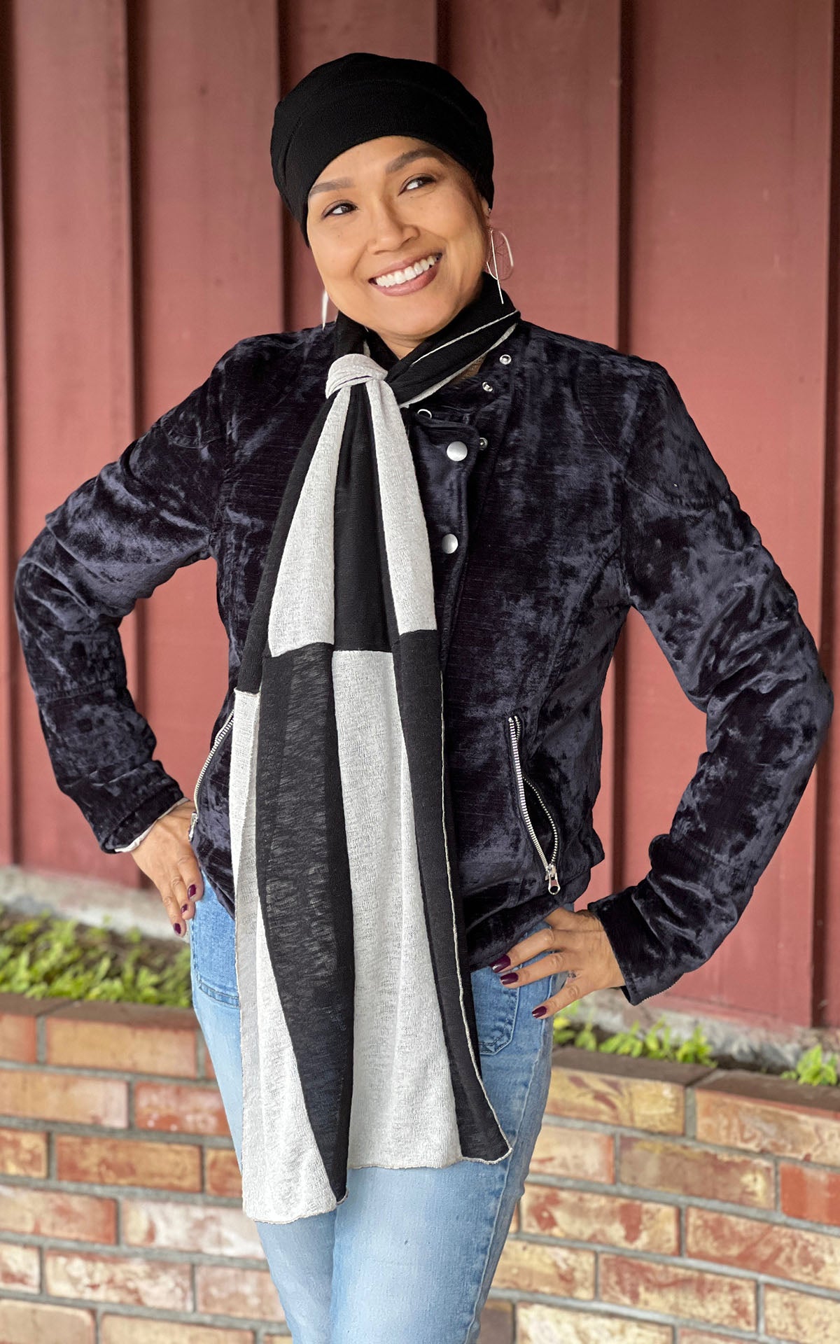 model in front of red wood and brick wall wearing a matching rowdie hat and  Upcycled Motley Scarf in the small pattern. Two colors, Sandstone and Scorpion in an alternating pattern. Handmade in Seattle, WA by Pandemonium Seattle.