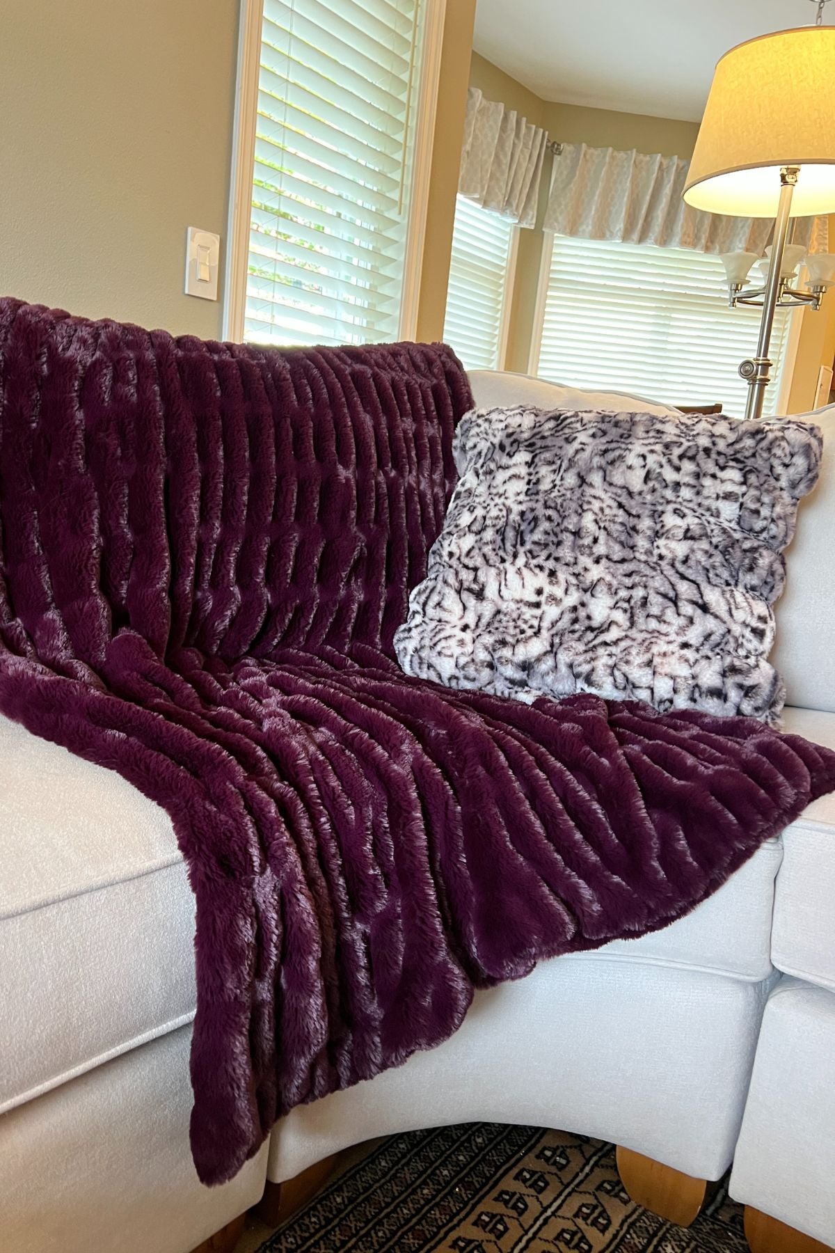 Draped over a chair is a Luxury Faux Fur Throw in Merlot with a Snow Leopard Pillow  From Royal Opulence Collection made by Pandemonium Seattle