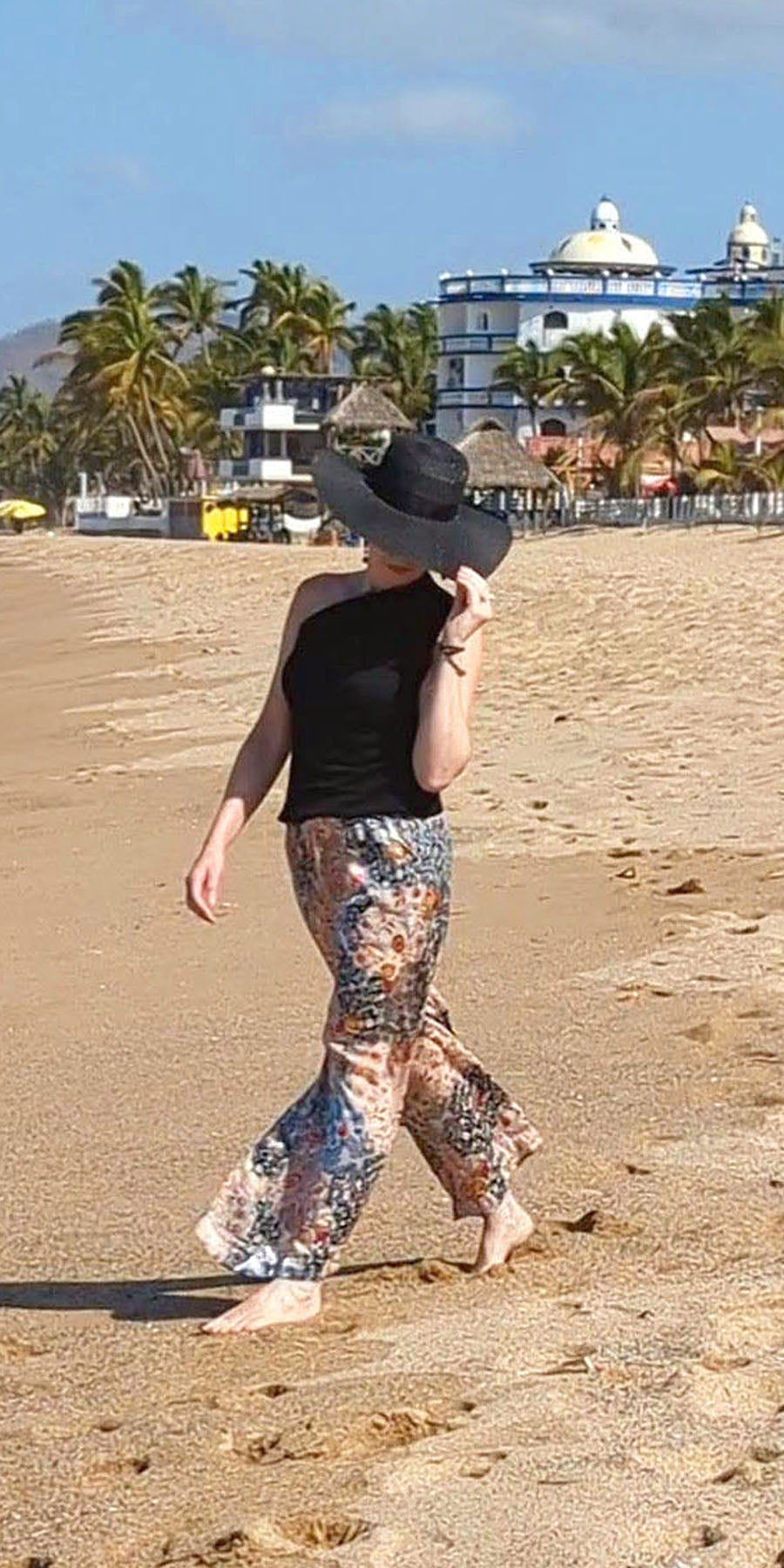 model walking on beach in floral silk palazzo pants with sun hat handmade in the USA by Leigh Young Collection a division of Pandemonium Seattle mobile view