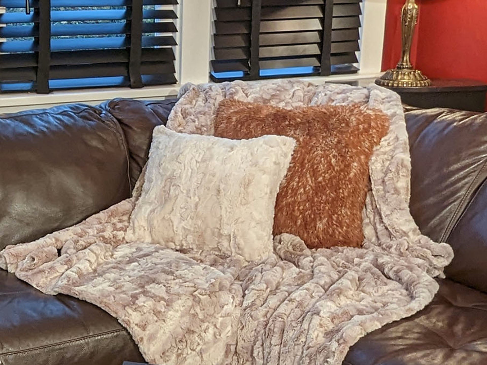 leather couch topped with a cream faux fur throw and pillow and a long hair orange pillow handmade in the USA by Pandemonium Seattle