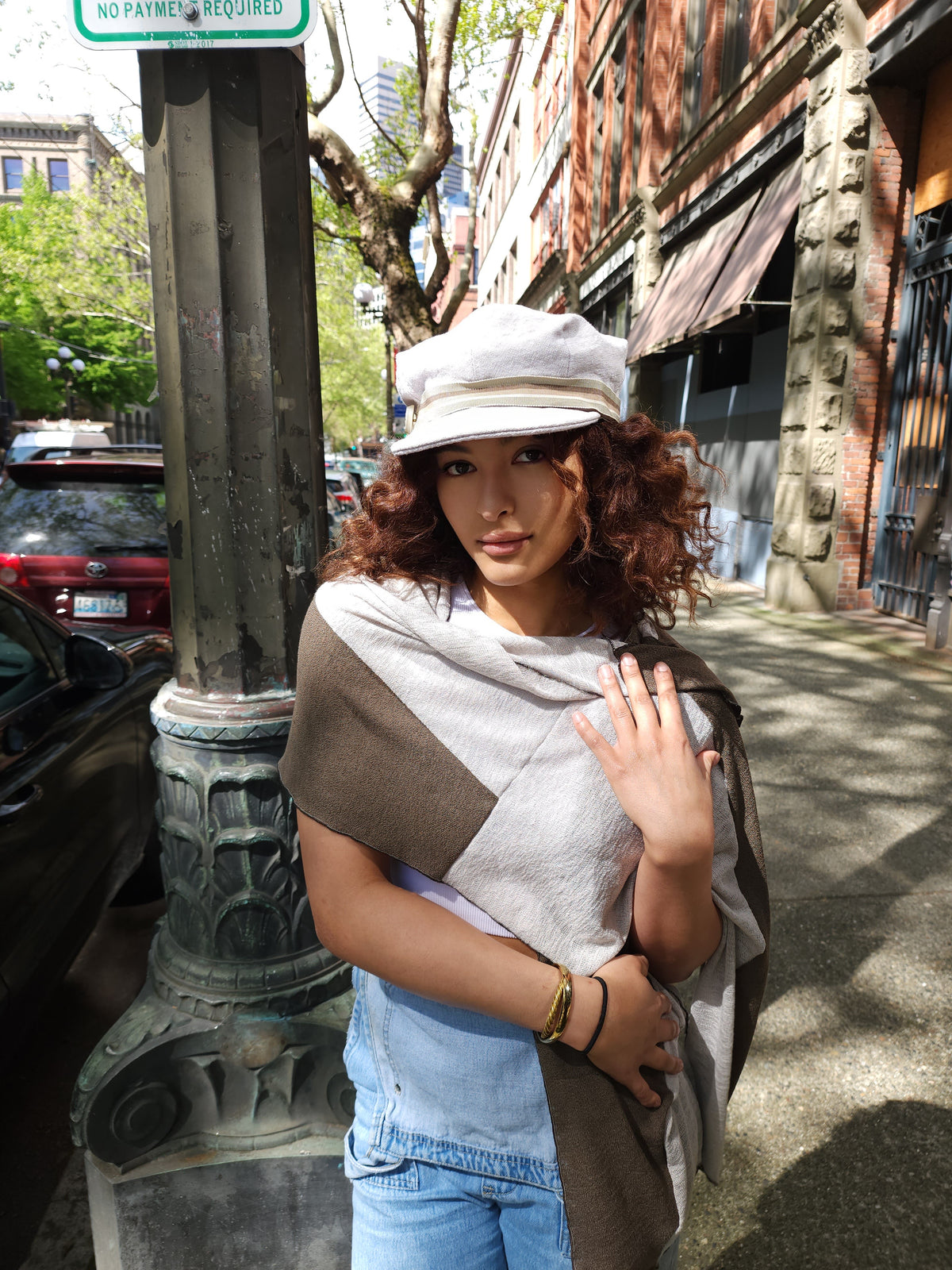 Model on street wearing Valerie cap hat and Upcycled Motley Scarf in Mezcal and Sandstone on Woman. Large pattern showing open around neck. Handmade in Seattle, WA.