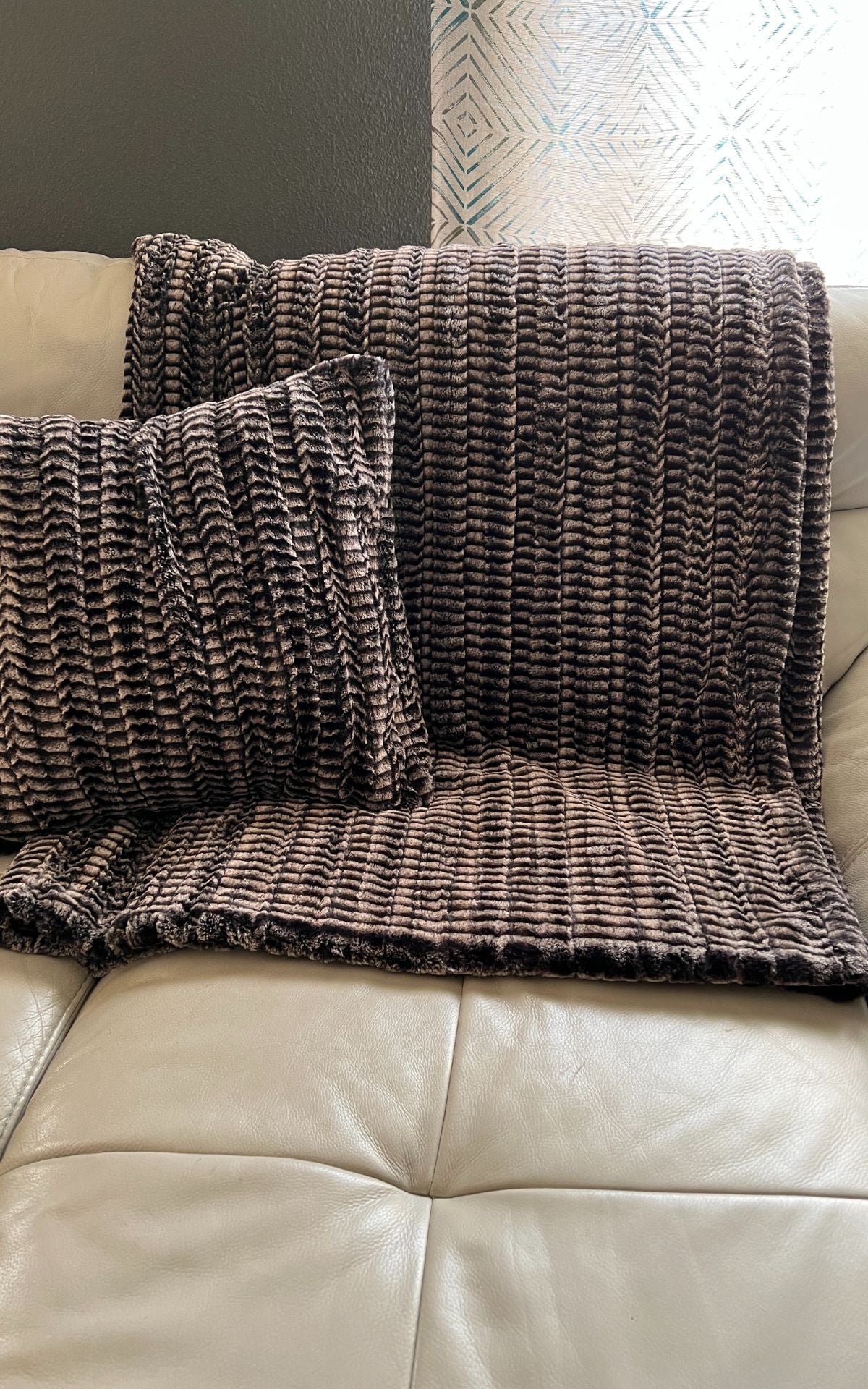 Faux fur throw in 8MM Sepia and matching throw pillow, on a cream sofa. Made in Seattle, WA, USA. Pandemonium Millinery