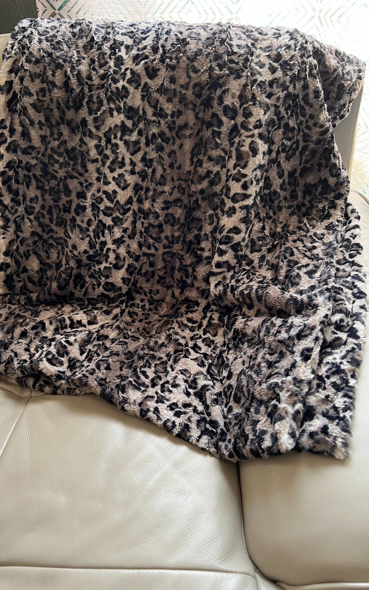 Faux Fur Throw in Savannah Cat, draped over back of a cream leather sofa. Made in Seattle, WA, USA. Pandemonium Seattle.