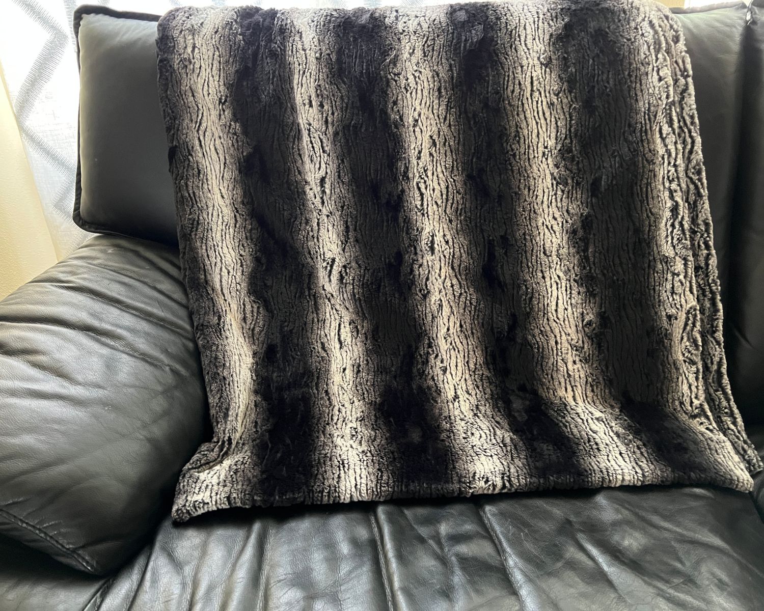 Faux fur throw in Smouldering Sequoia draped over back of black leather sofa. Made in Seattle, WA, USA. Pandemonium Millinery.