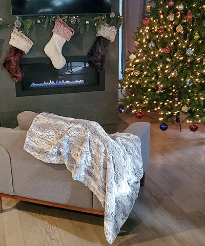 Throw in Luxury Faux Fur in  Winter River; Ice Blue  Ivory  on couch by stocking , Christmas tree and fireplace | Luxury Faux Fur  | Pandemonium Millinery