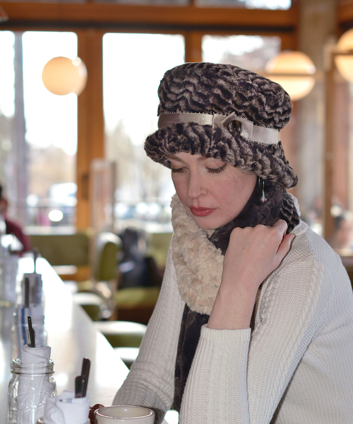 Woman in a Café wearing  Molly Bucket Style Hat in 8mm in  Sepia Faux Fur with Pico Satin Band featuring a Carmel Lucite Button |Handmade By Pandemonium Millinery | Seattle WA USA